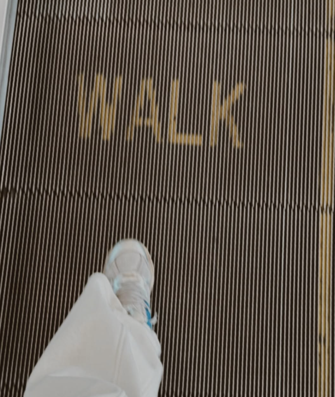 View of a person's white sneaker and pants walking on a brown striped mat with the word 'WALK' written on it.