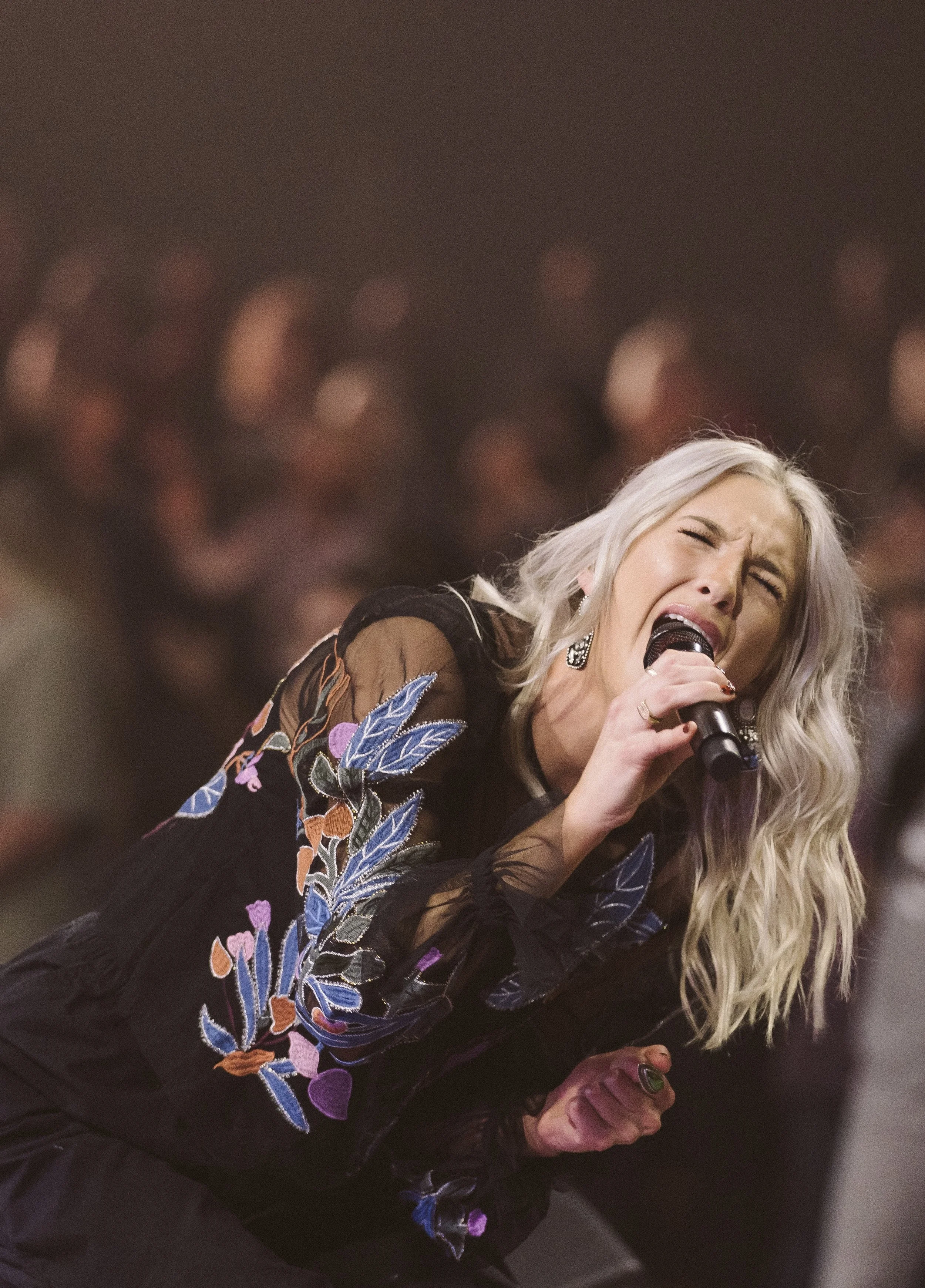 A woman with long blonde hair singing passionately into a microphone during a live performance.