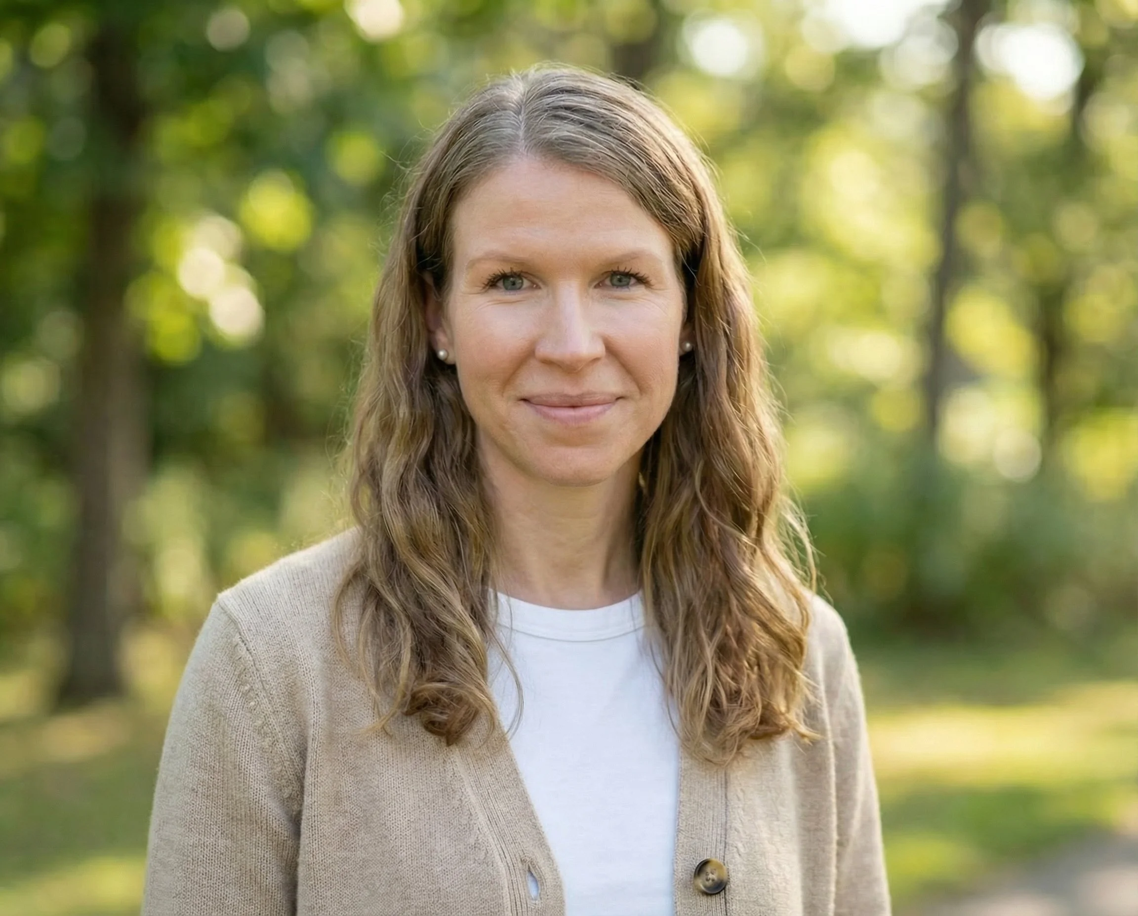 A woman with long wavy hair smiling outdoors in a green park.