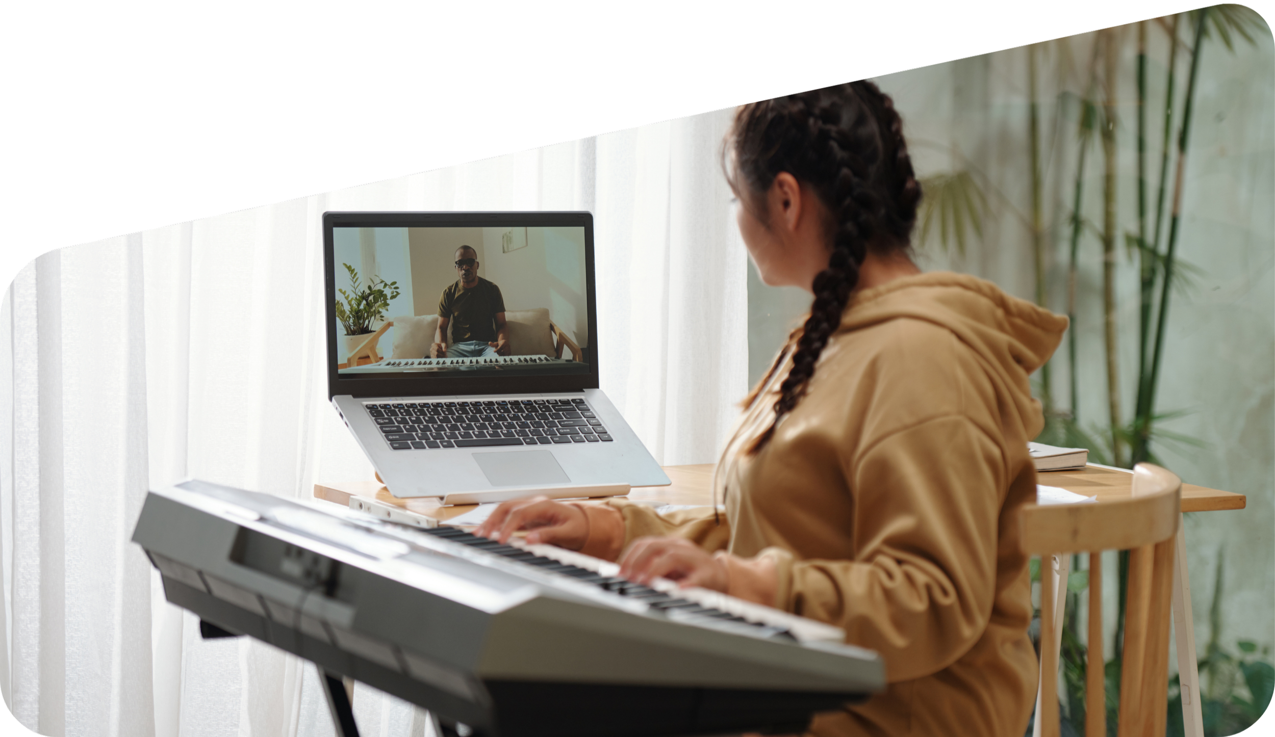 A woman playing a keyboard while video chatting with a man on her laptop, with a plant and curtains in the background.