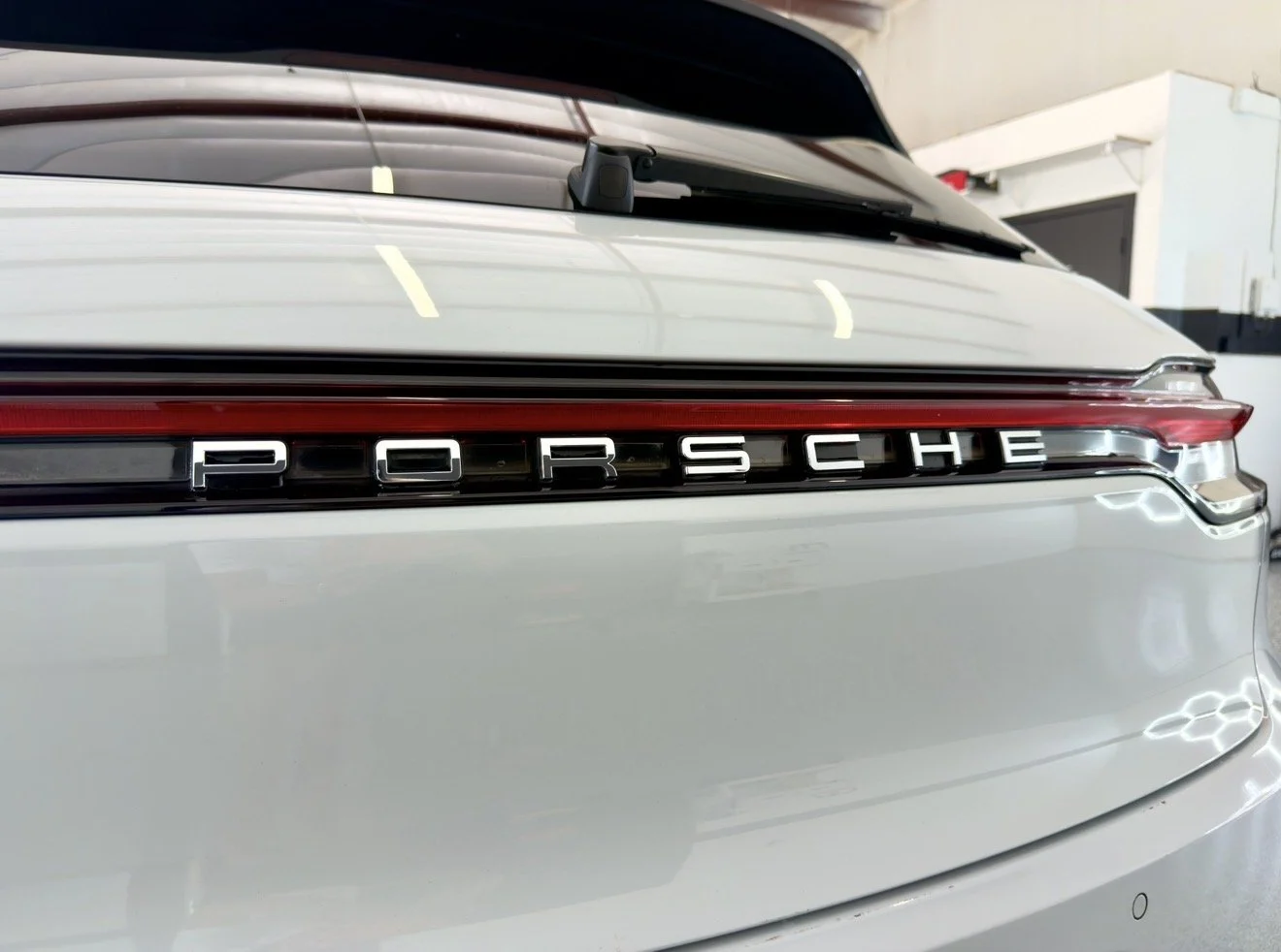 The rear end of a white Porsche car, showing the Porsche logo on the back of the vehicle.