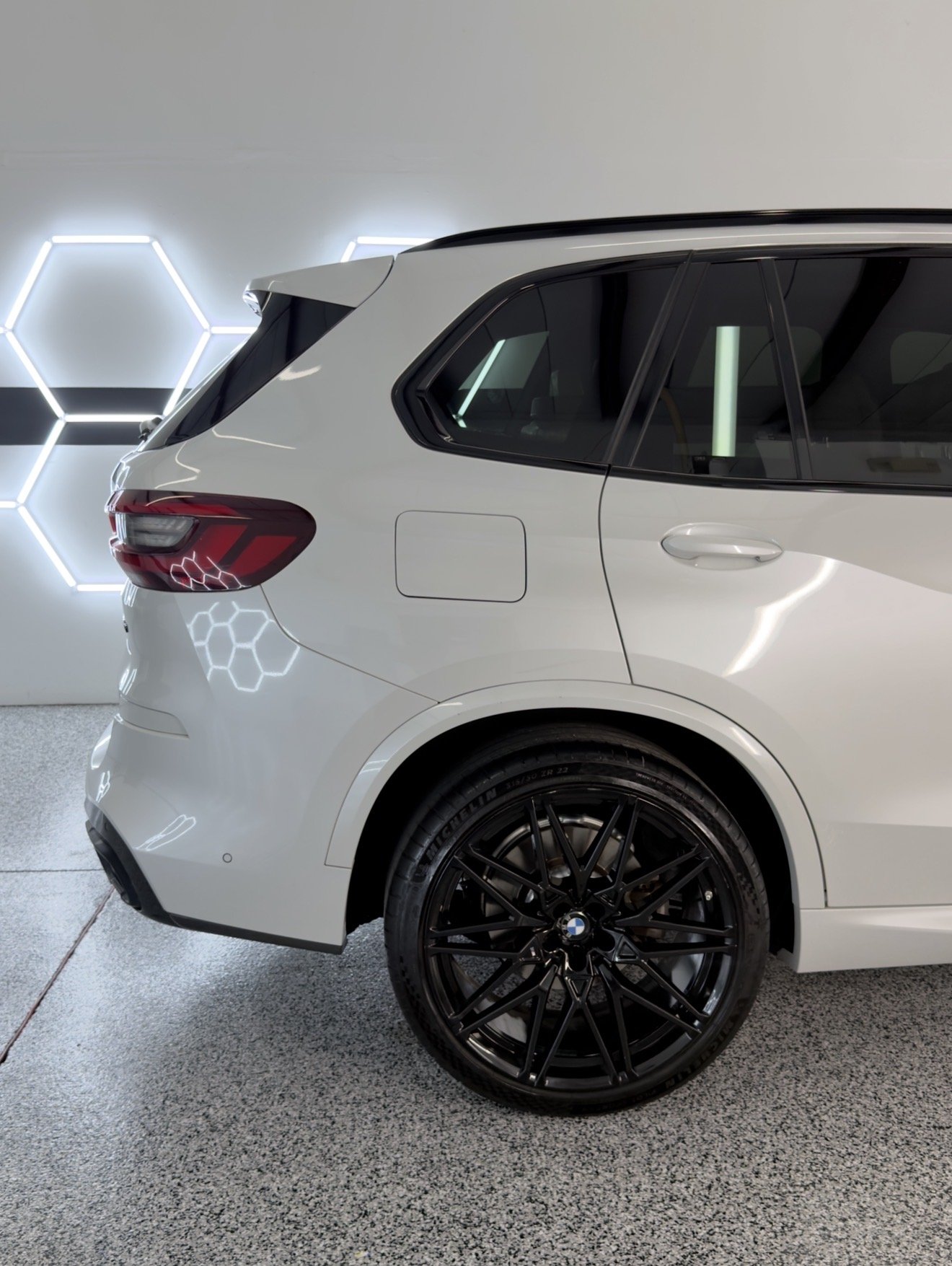 White luxury SUV with black wheels parked indoors against a wall with illuminated hexagon patterns.