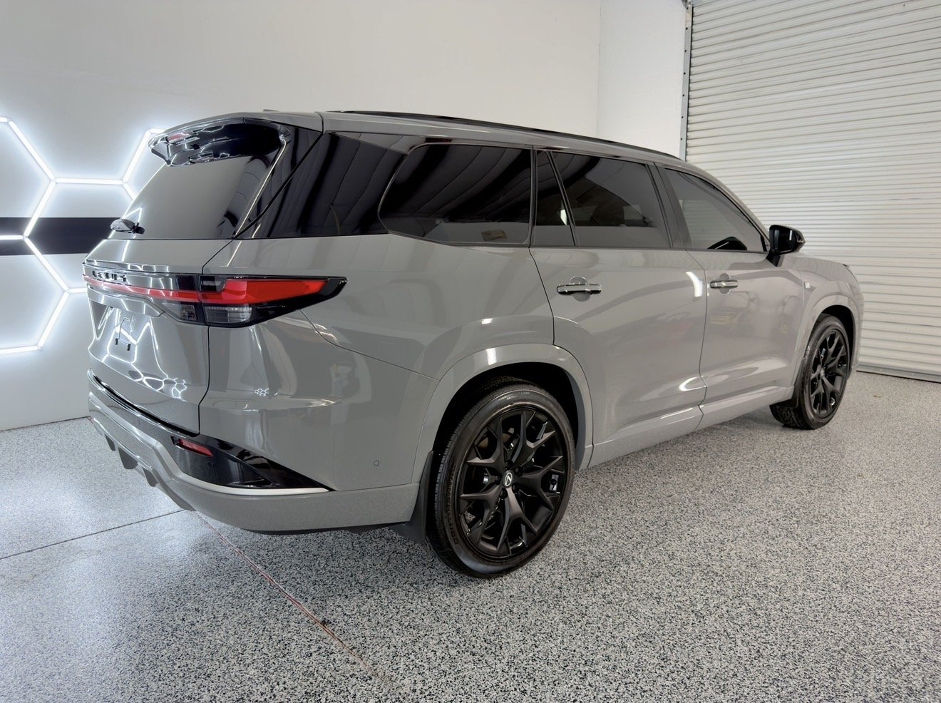 A silver SUV parked indoors near a white wall with hexagonal LED lights, featuring tinted windows and black alloy wheels.