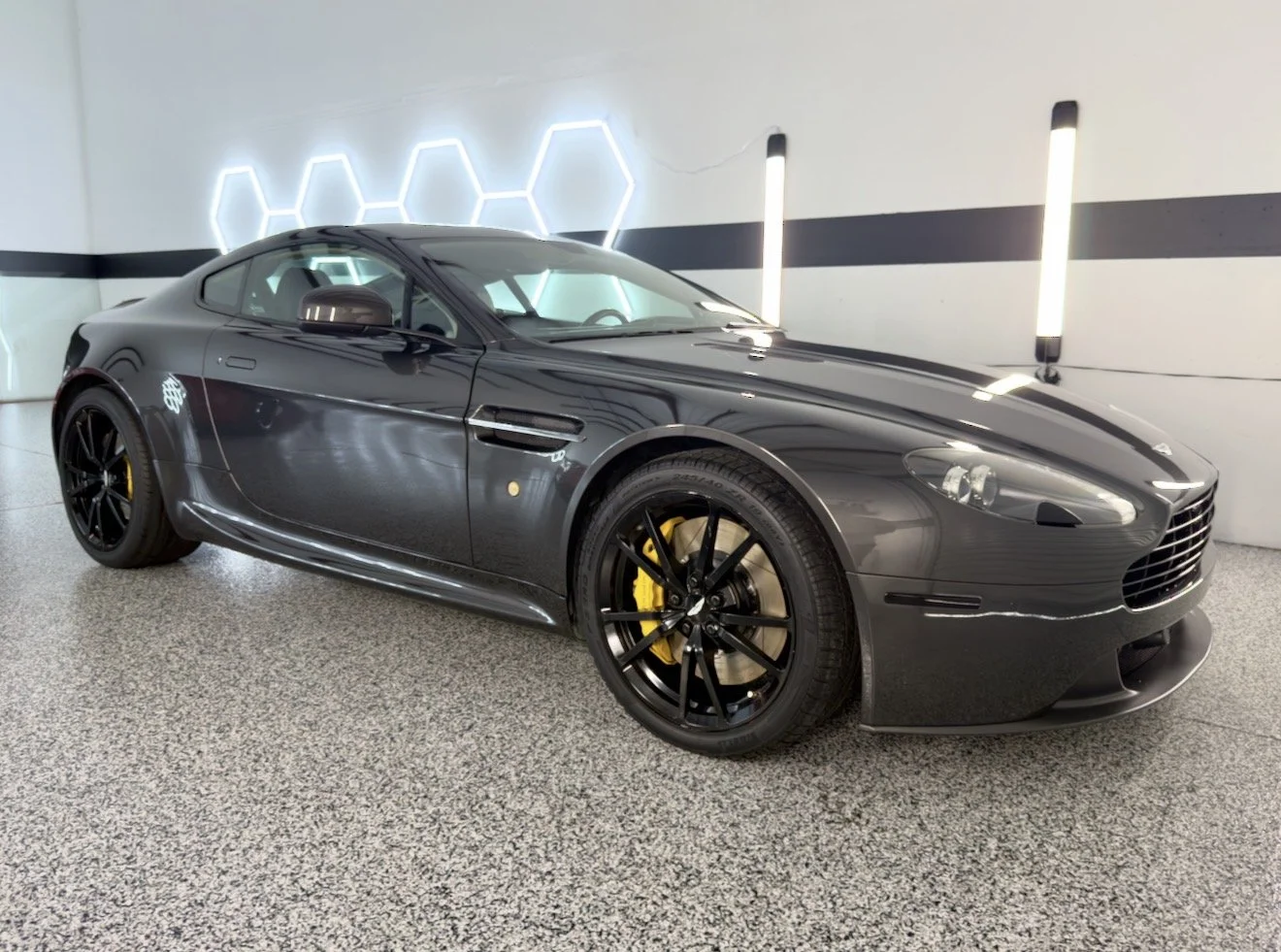 Black sports car with yellow brake calipers parked indoors in a modern, well-lit garage.
