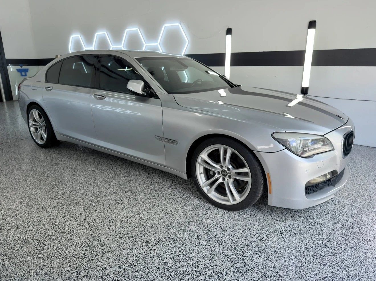Silver luxury sedan car parked indoors with black and white walls and LED lights.