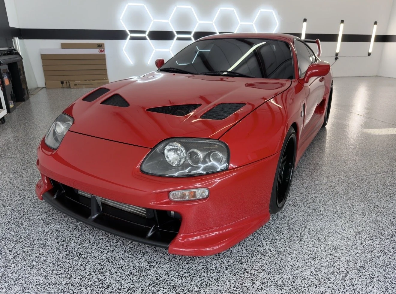 Red sports car inside a garage with hexagon shaped lights on the wall.