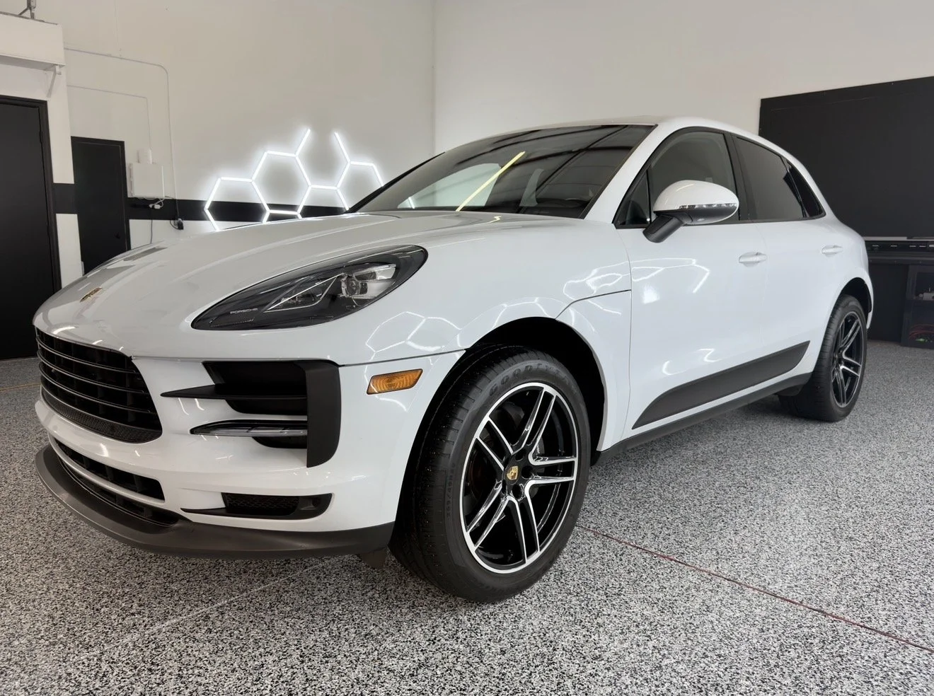 white Porsche SUV inside a showroom with black and white geometric wall decorations.