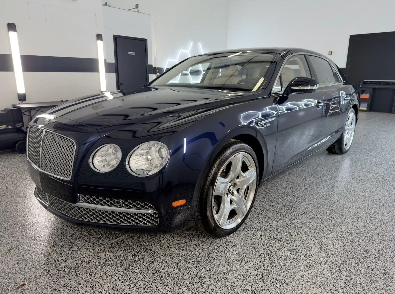 A black luxury sedan in a showroom with glossy finish, distinctive grille, and alloy wheels.