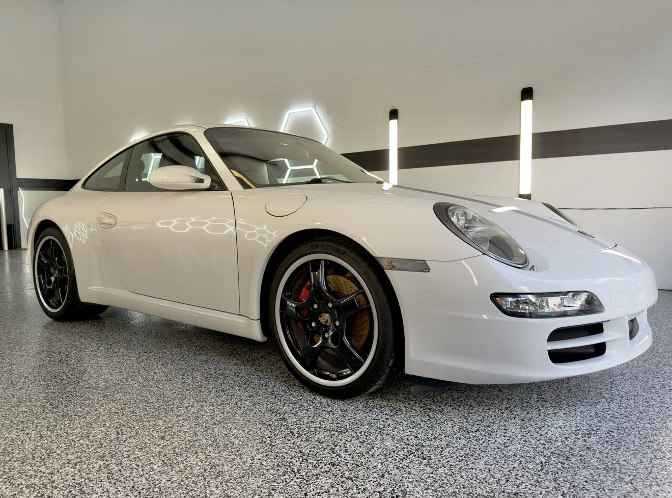 White Porsche sports car displayed indoors with black wheels and yellow brake calipers.