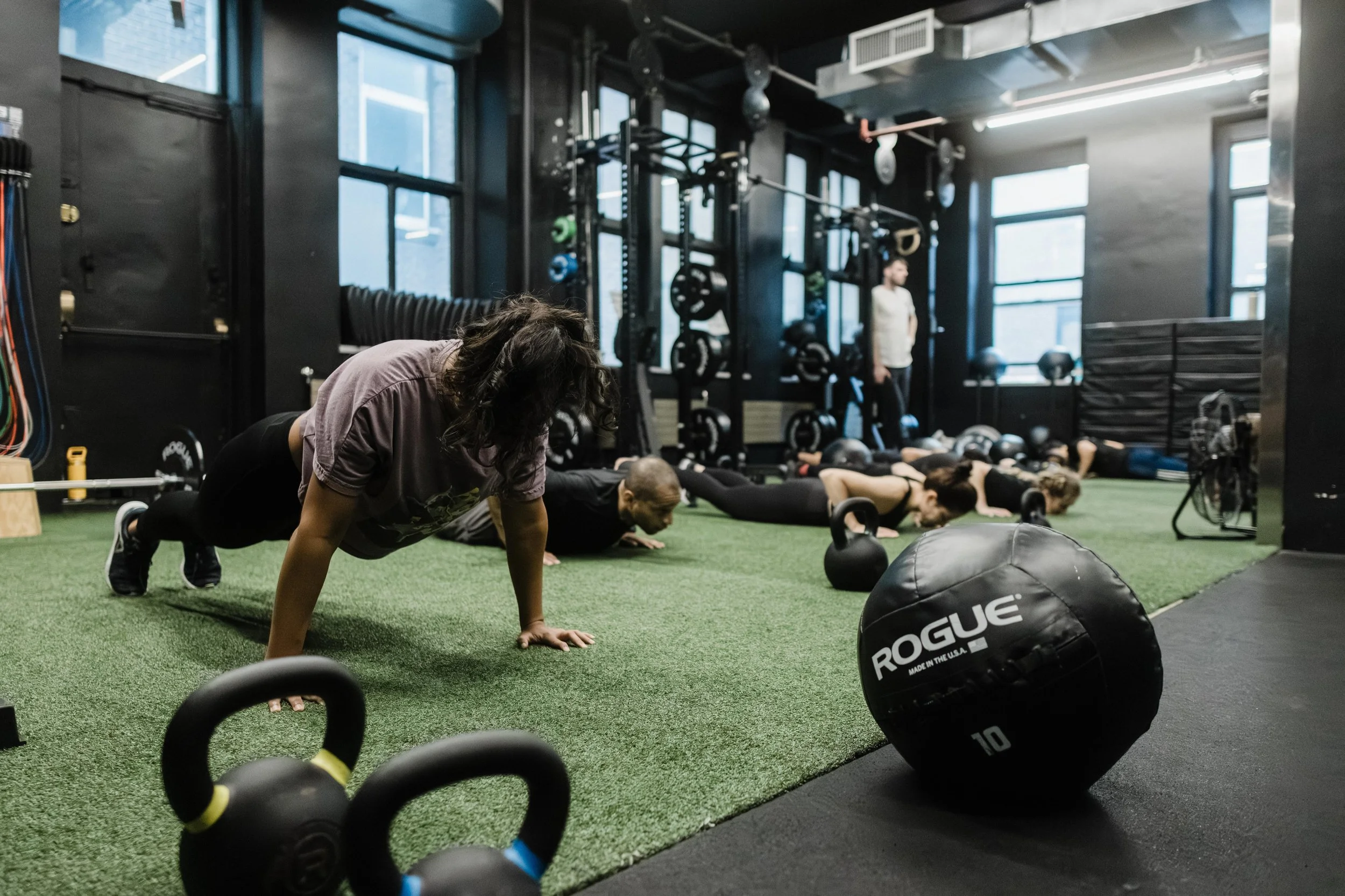People performing push-ups in a gym with fitness equipment and black walls.