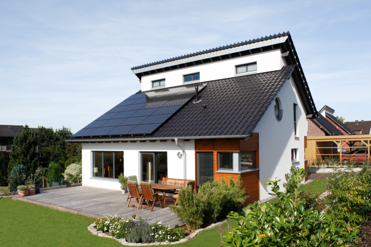 Ein modernes Haus mit Solarzellen auf dem Dach und einer Terrasse im Garten.