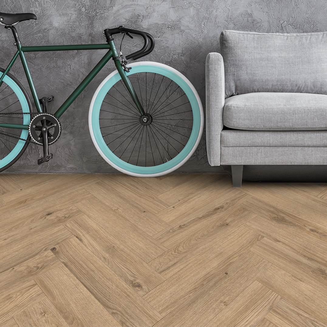 A green bicycle with aqua and white wheels, placed next to a gray sofa against a textured gray wall on a light wood floor.