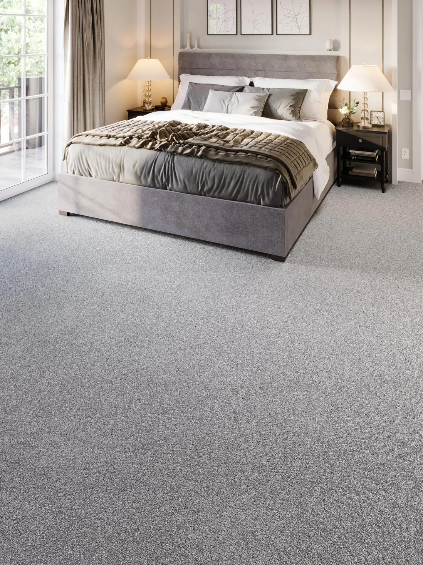 A neatly made bed with gray bedding and pillows, two nightstands with lamps on each side, and framed artwork on the wall in a bright bedroom with a sliding glass door leading to an outdoor area.