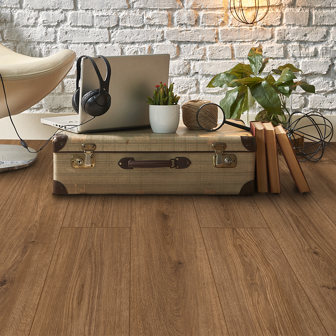A vintage suitcase on a wooden floor with a laptop, headphones, potted cactus, and books on top, and plants and string lights in the background.