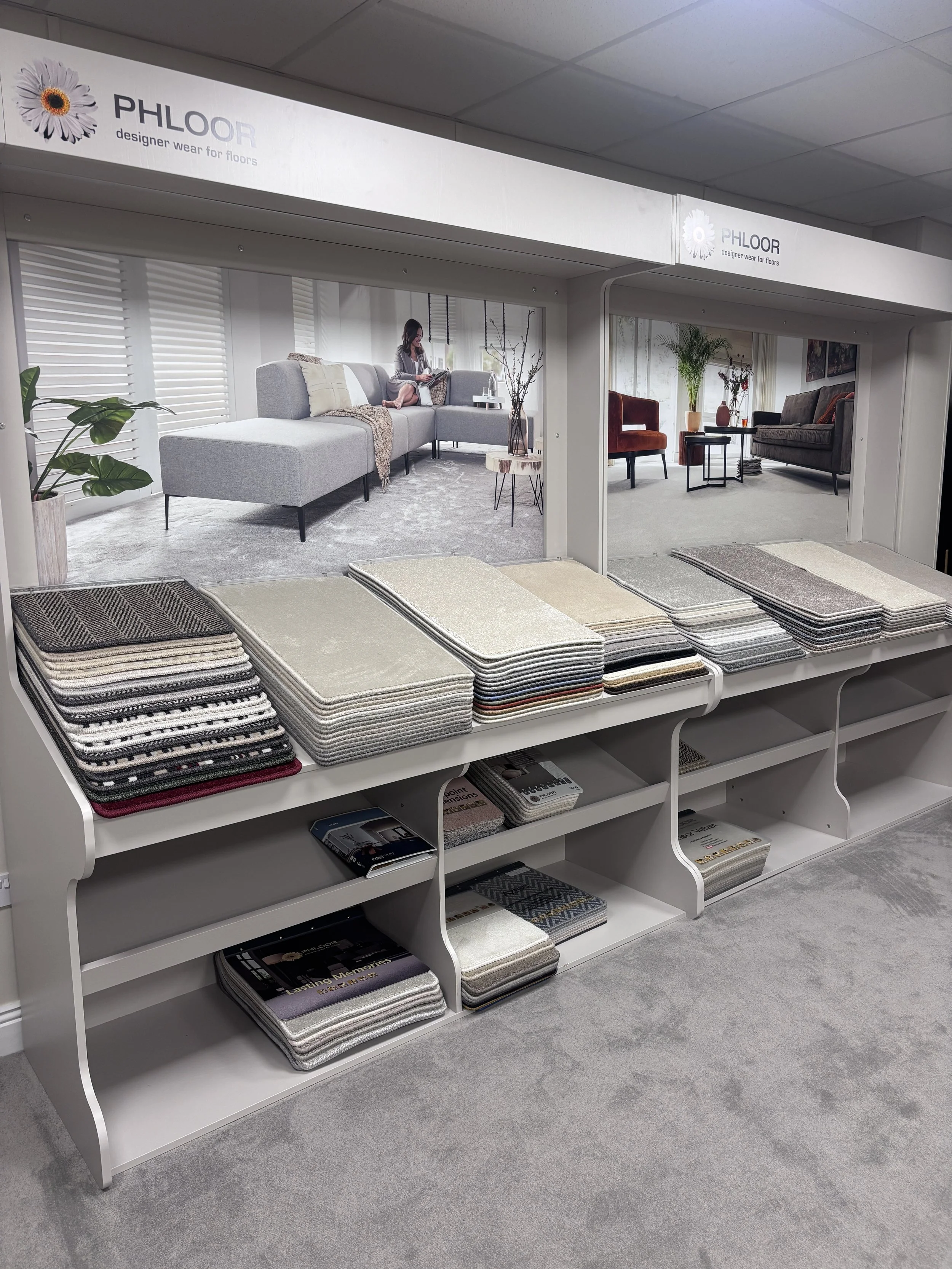 Display of fabric swatches and samples in front of a showroom backdrop with images of interior living rooms and furniture.