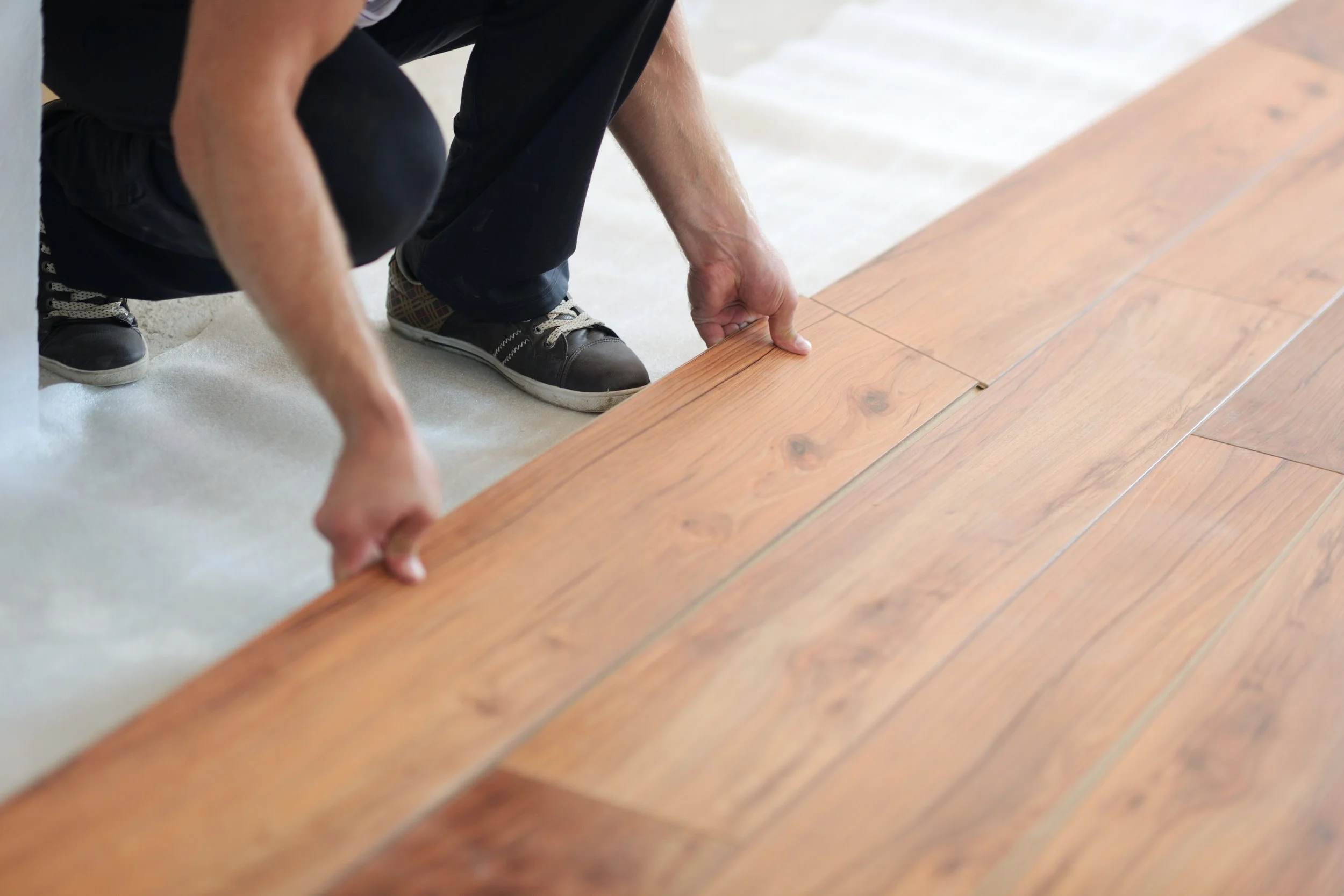 A person installing or adjusting a wooden floor, crouched down on the floor, handling a floorboard.