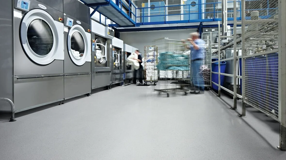 Laundromat with washing machines, people loading laundry and a cart with laundry, in a commercial laundry facility.