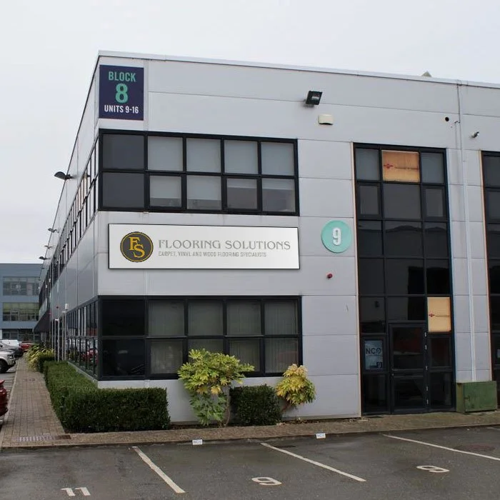 Exterior of a modern commercial building with signs for 'Flooring Solutions' and a numbered parking lot.