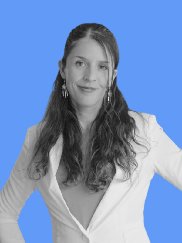 Black and white portrait of a woman with long wavy hair wearing a white blazer and earrings, against a blue background.