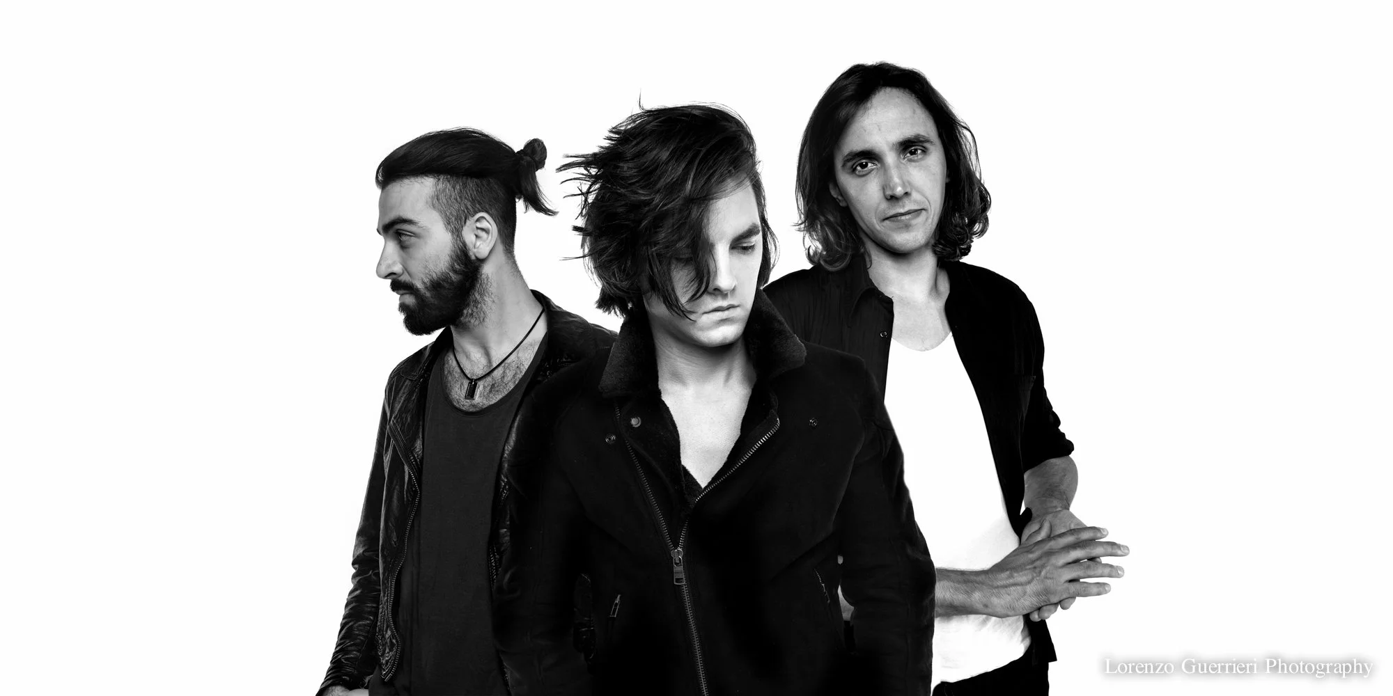 Black and white photo of three people, a woman in the front and two men behind her, with serious expressions, standing against a plain white background.