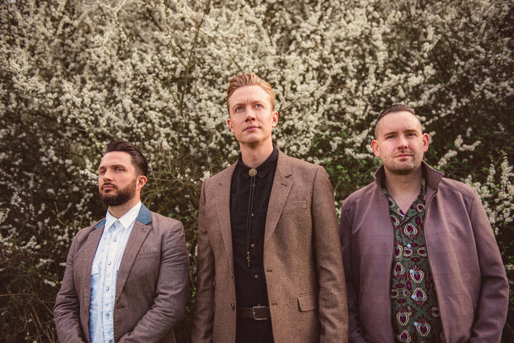 Three men standing outside in front of a flowering bush.