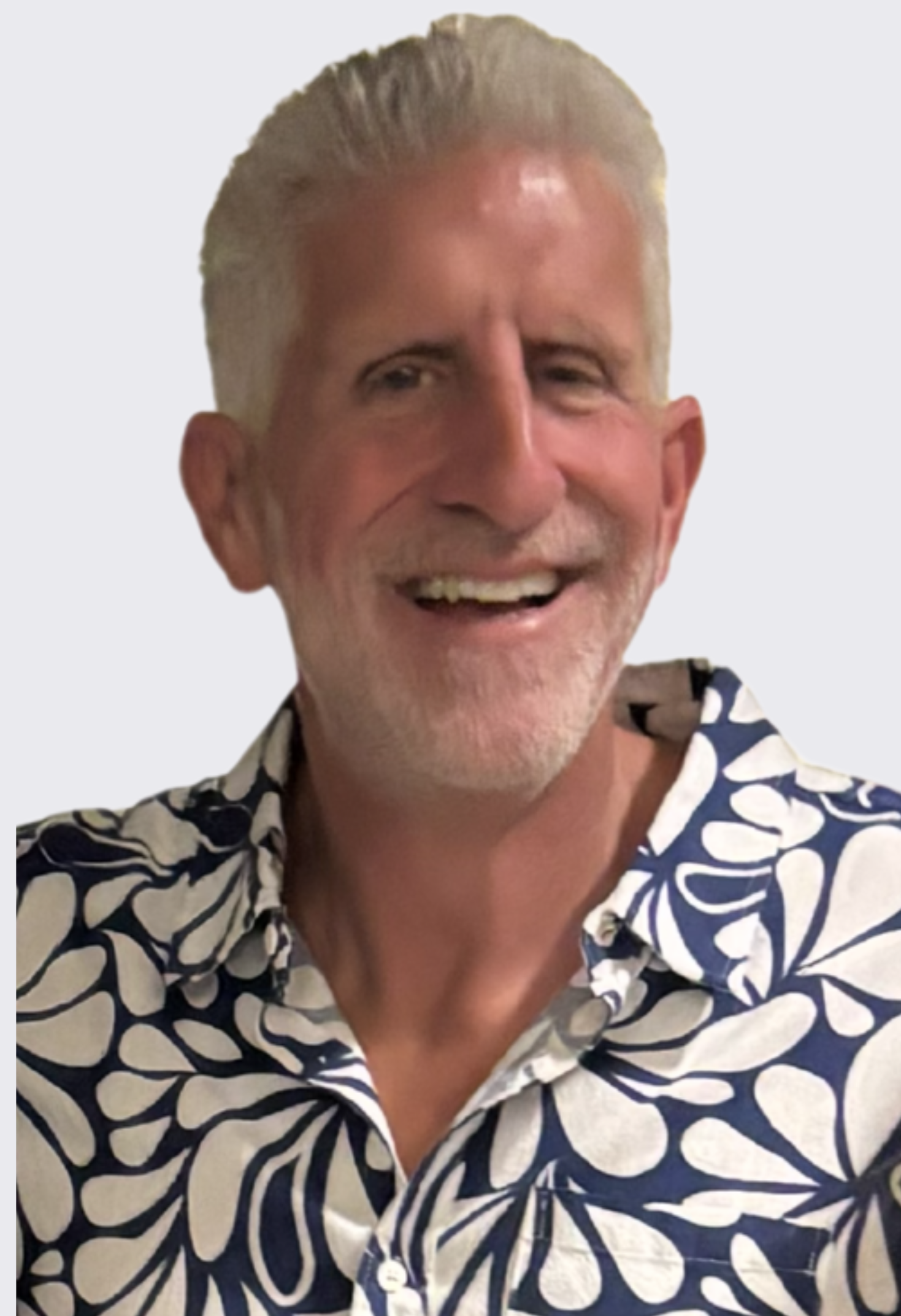 A smiling older man with short, gray hair and a beard, wearing a navy and white patterned shirt, against a plain light-colored background.