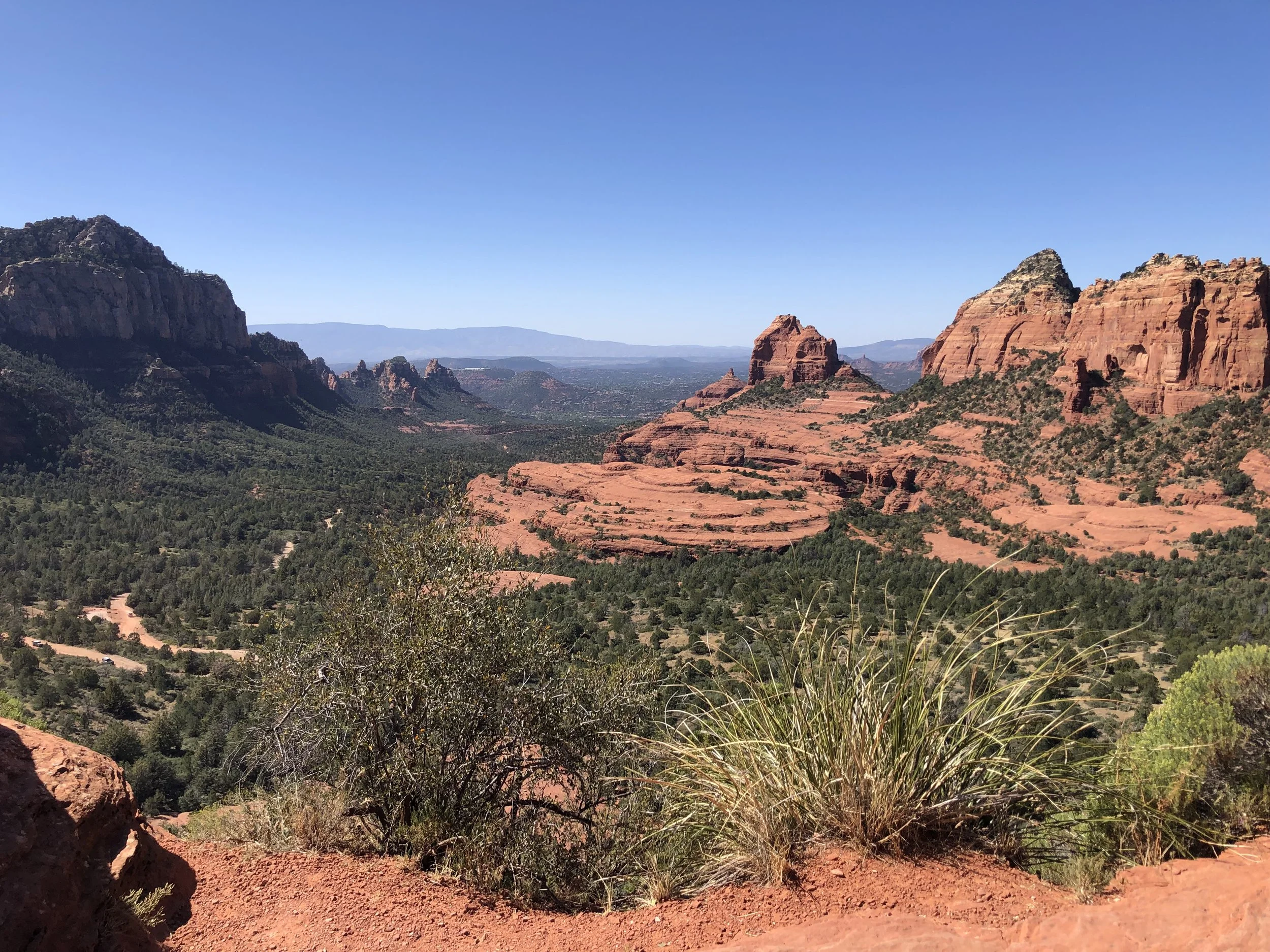 Scenic view of red rock formations and green desert vegetation under a clear blue sky.