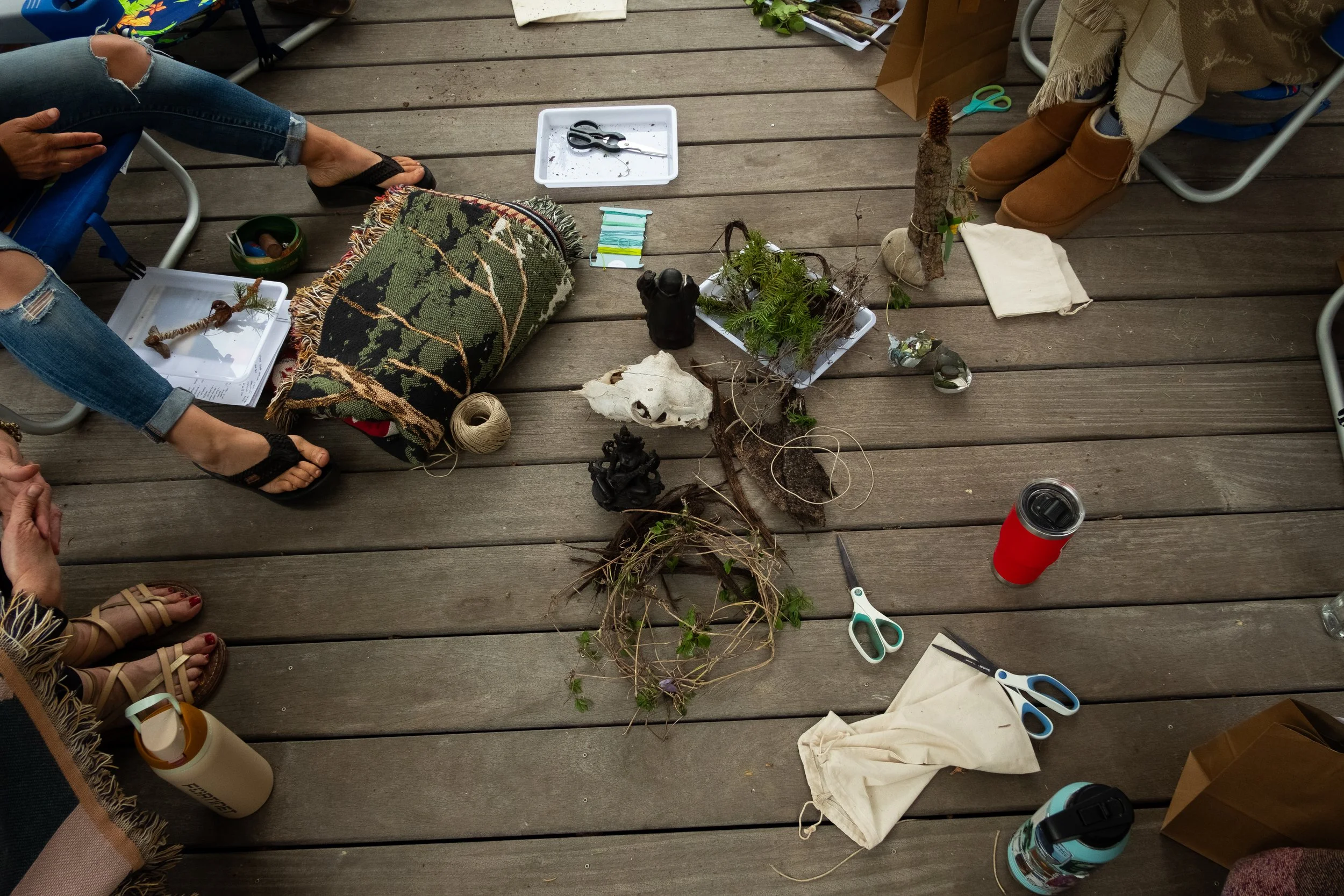 Top view of a wooden table with various items including gardening tools, plants, scissors, a rocks, a blanket, paper, a coffee cup, and other miscellaneous objects.
