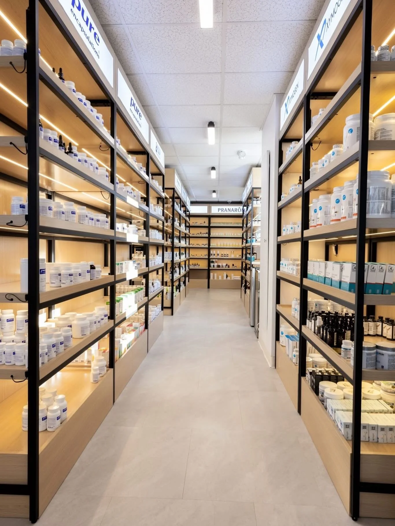 Rayonnages de pharmacie avec des bocaux et des flacons de médicaments. Script 'PURE' visible sur les panneaux au plafond.