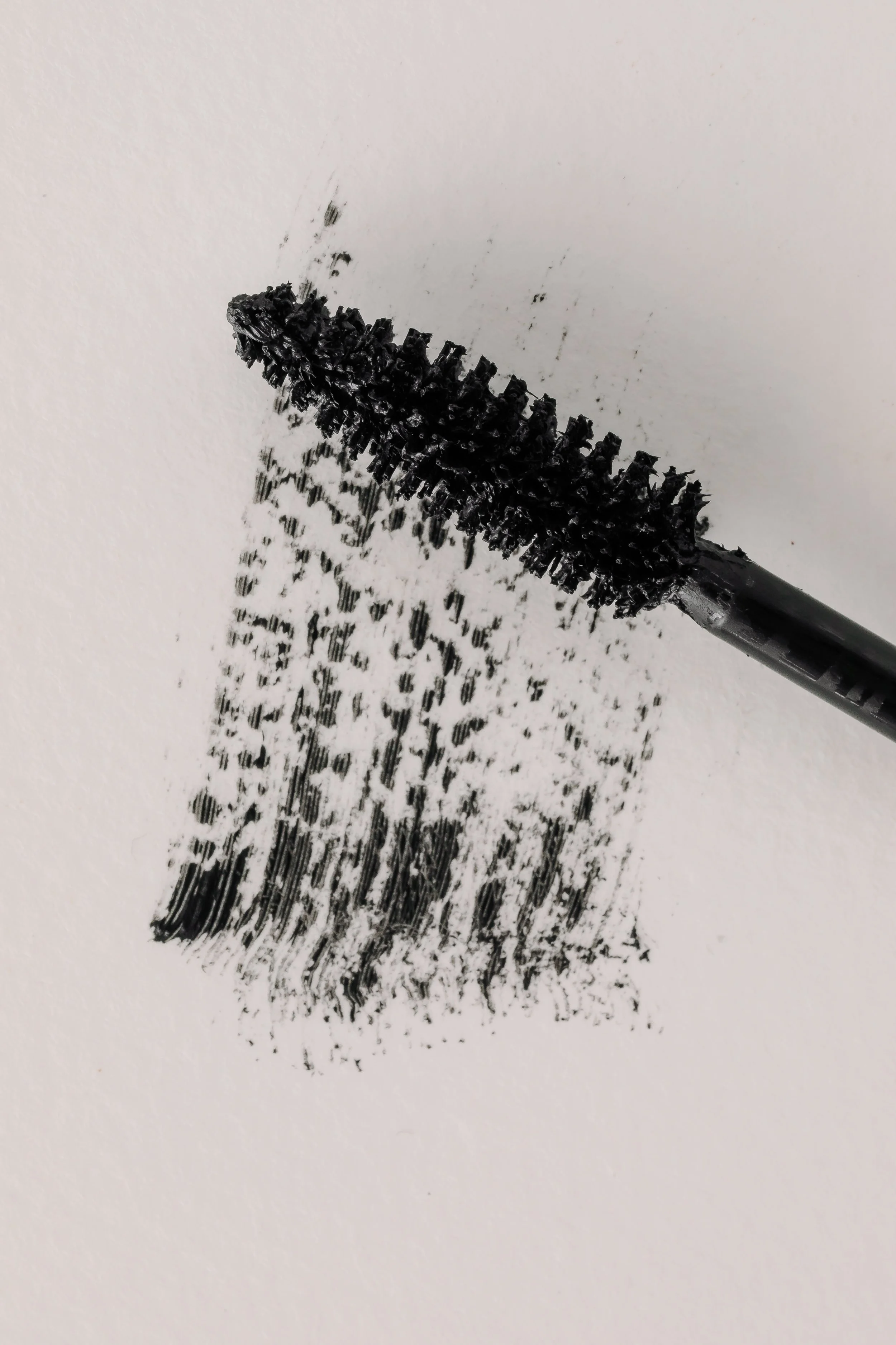 Black mascara wand smudging ink on a white paper surface.