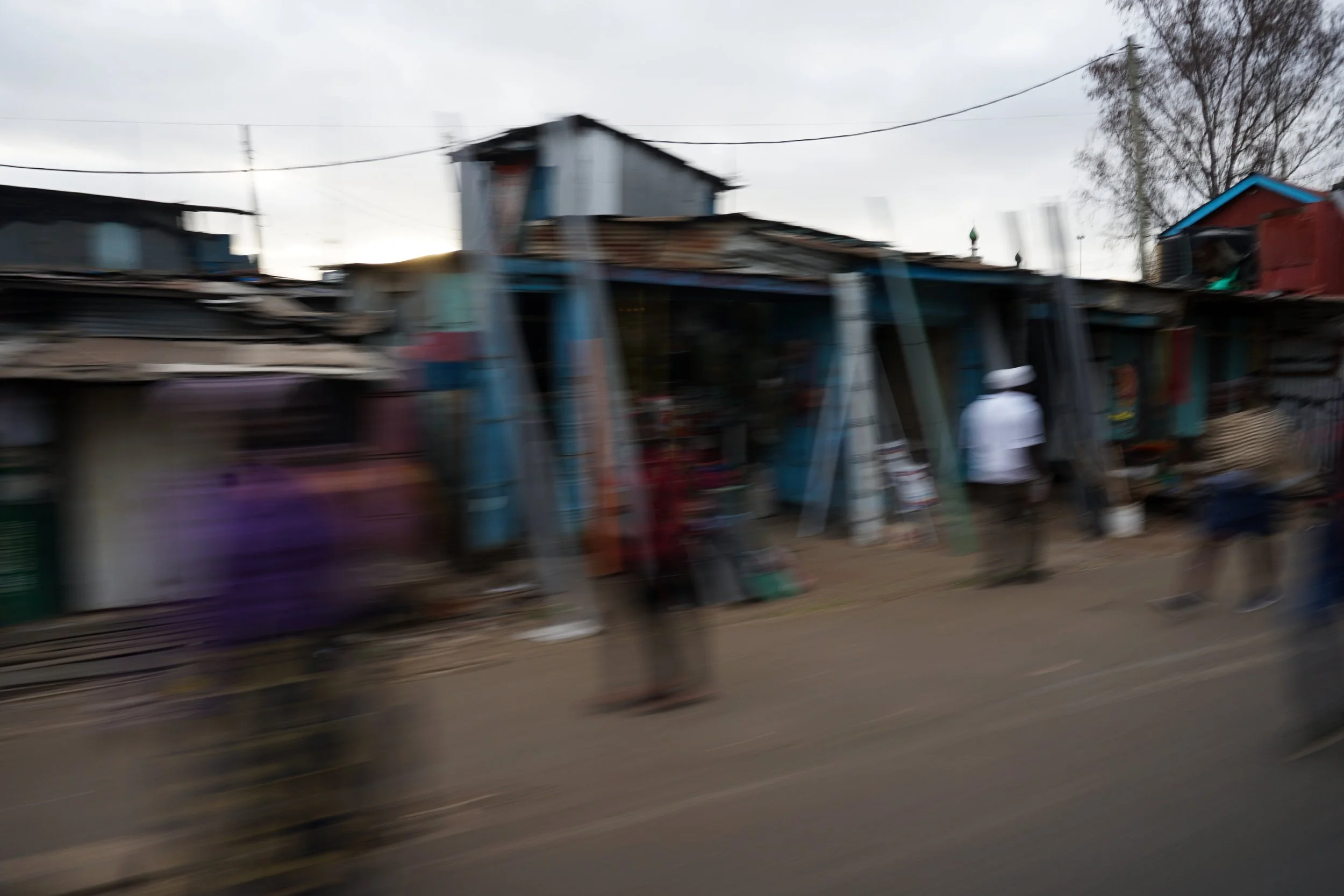 Blurry image of a street scene with small shops and people walking, possibly in an urban or market area.