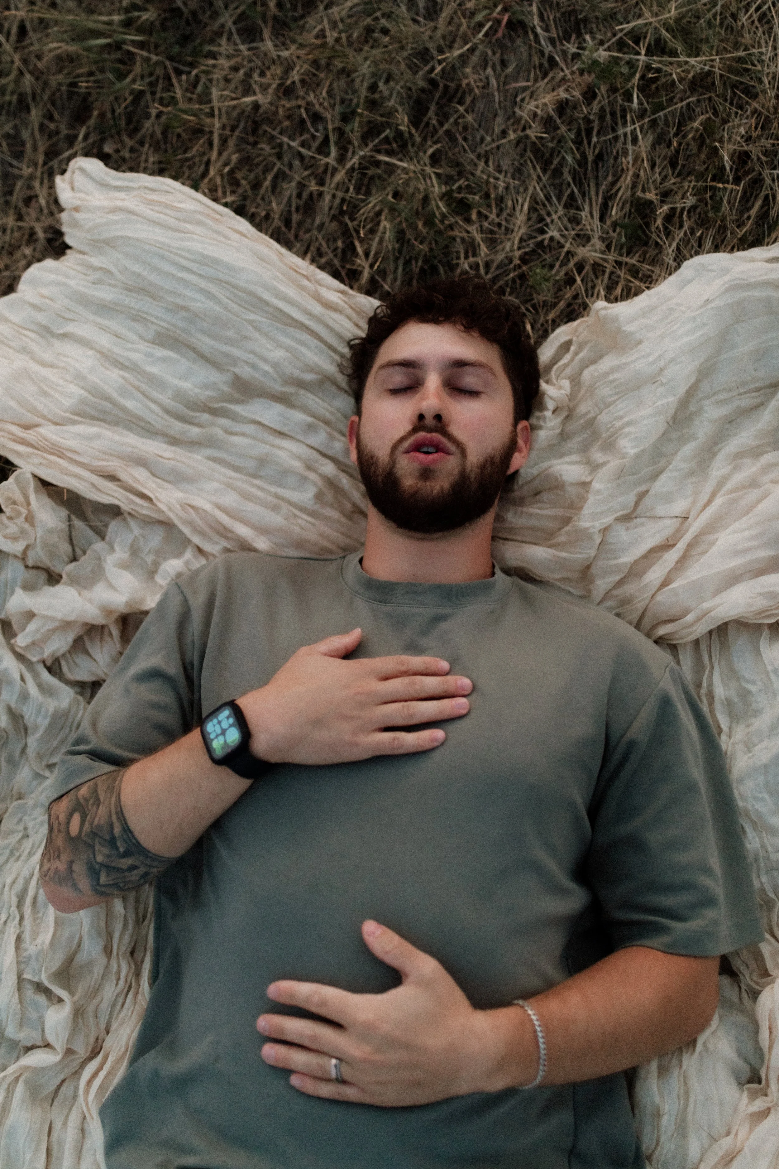 A young man laying down practicing breathwork  with one hand on his chest and one hand on his belly