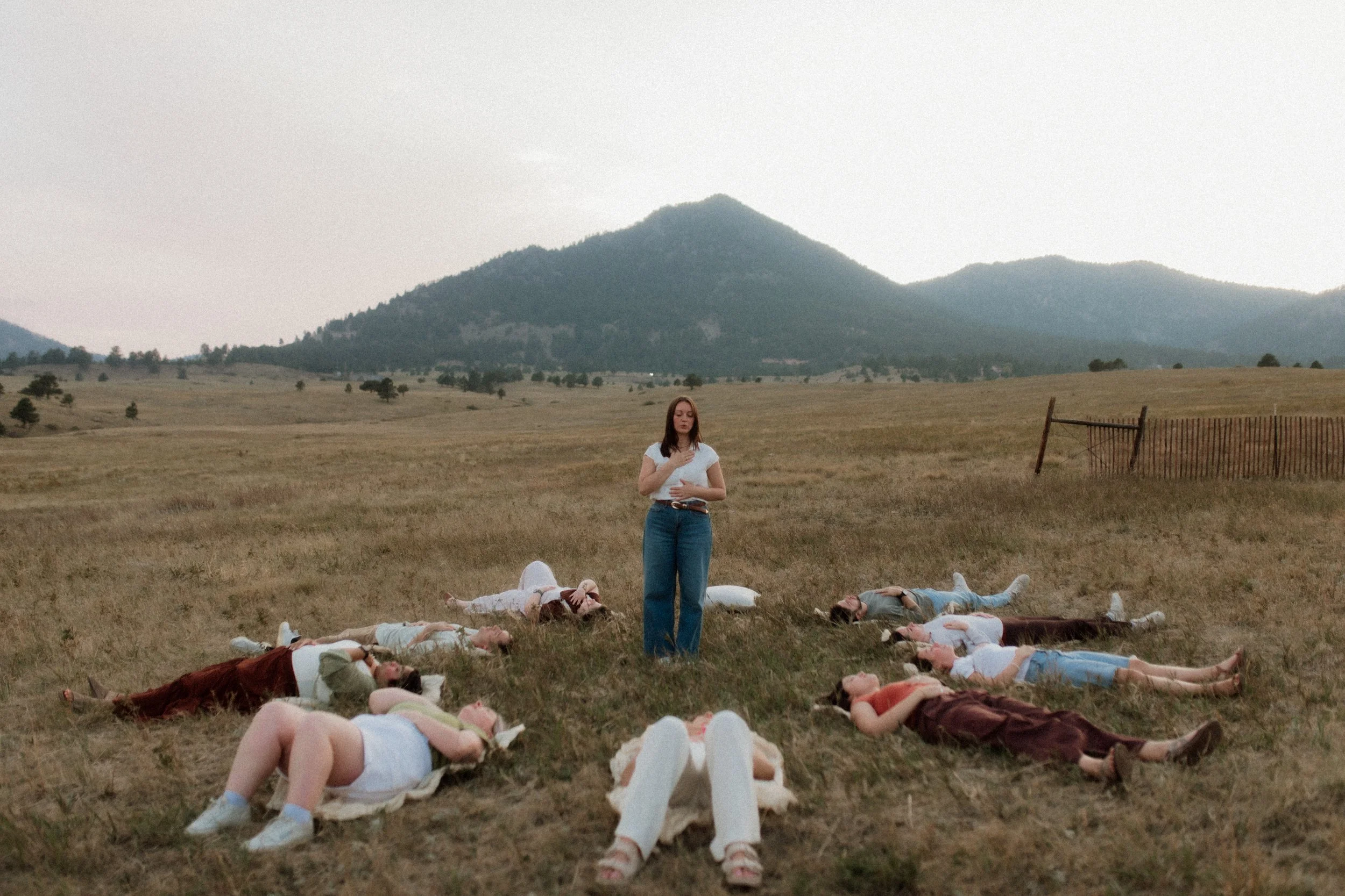 A woman with her hands over her heart and belly teaching breathwork  to a group of people around her