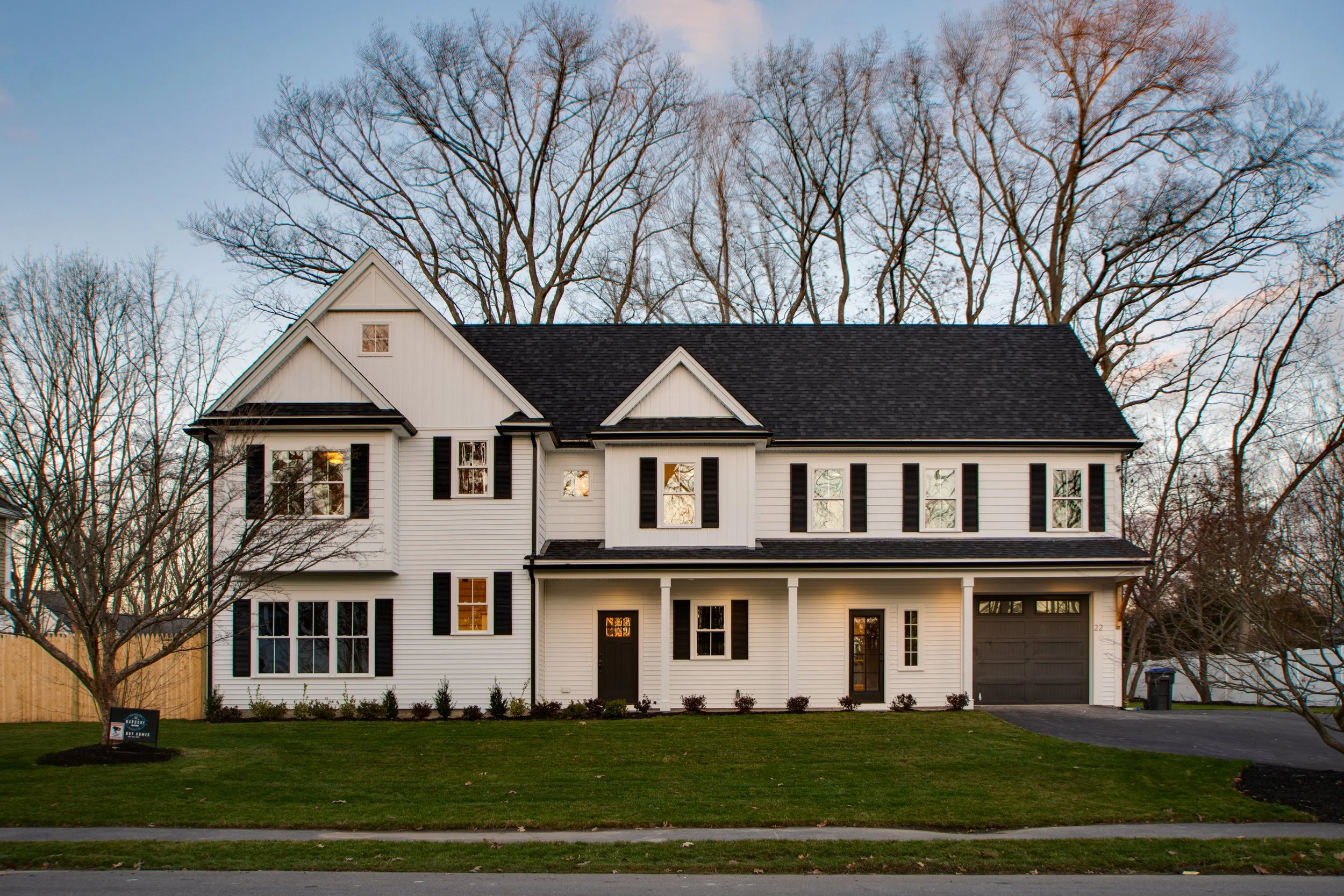Exterior view of a large white two-story house with black shutters, a dark roof, and a front porch, surrounded by leafless trees and a well-maintained lawn.