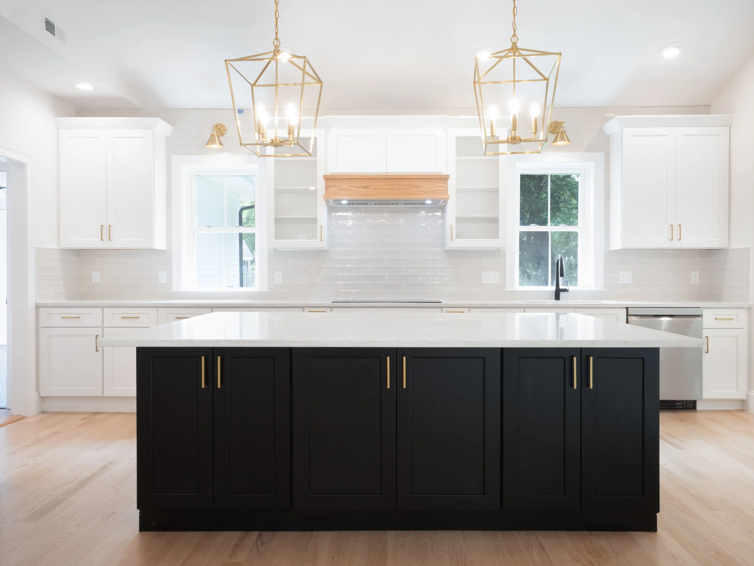Modern kitchen with white cabinets, black island, pendant lighting, light hardwood floor, and stainless steel appliances.