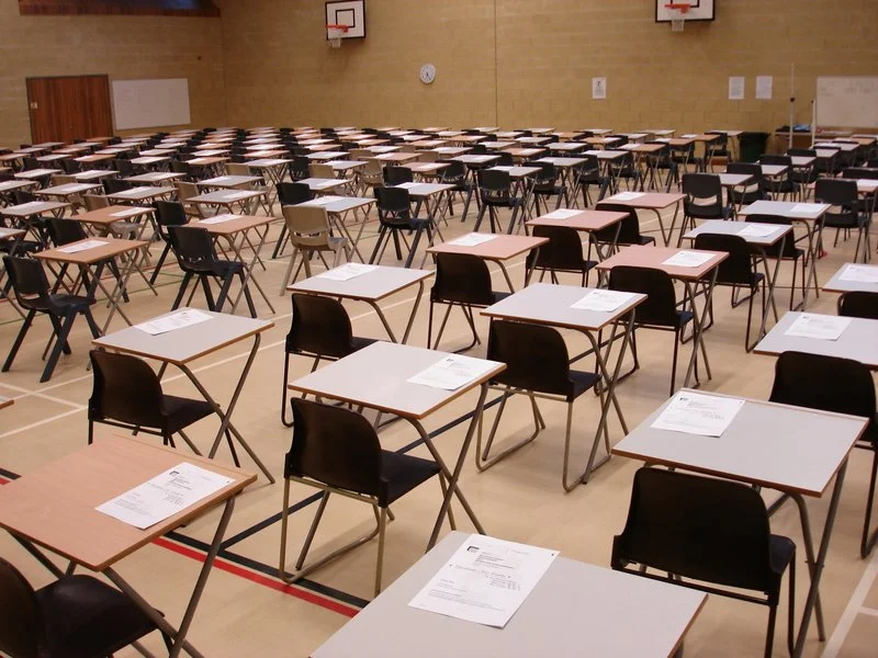 Rows of desks and chairs set up in an exam hall, prepared for GCSE or A Level pupils who will enter to undertake their public examinations/assessments.