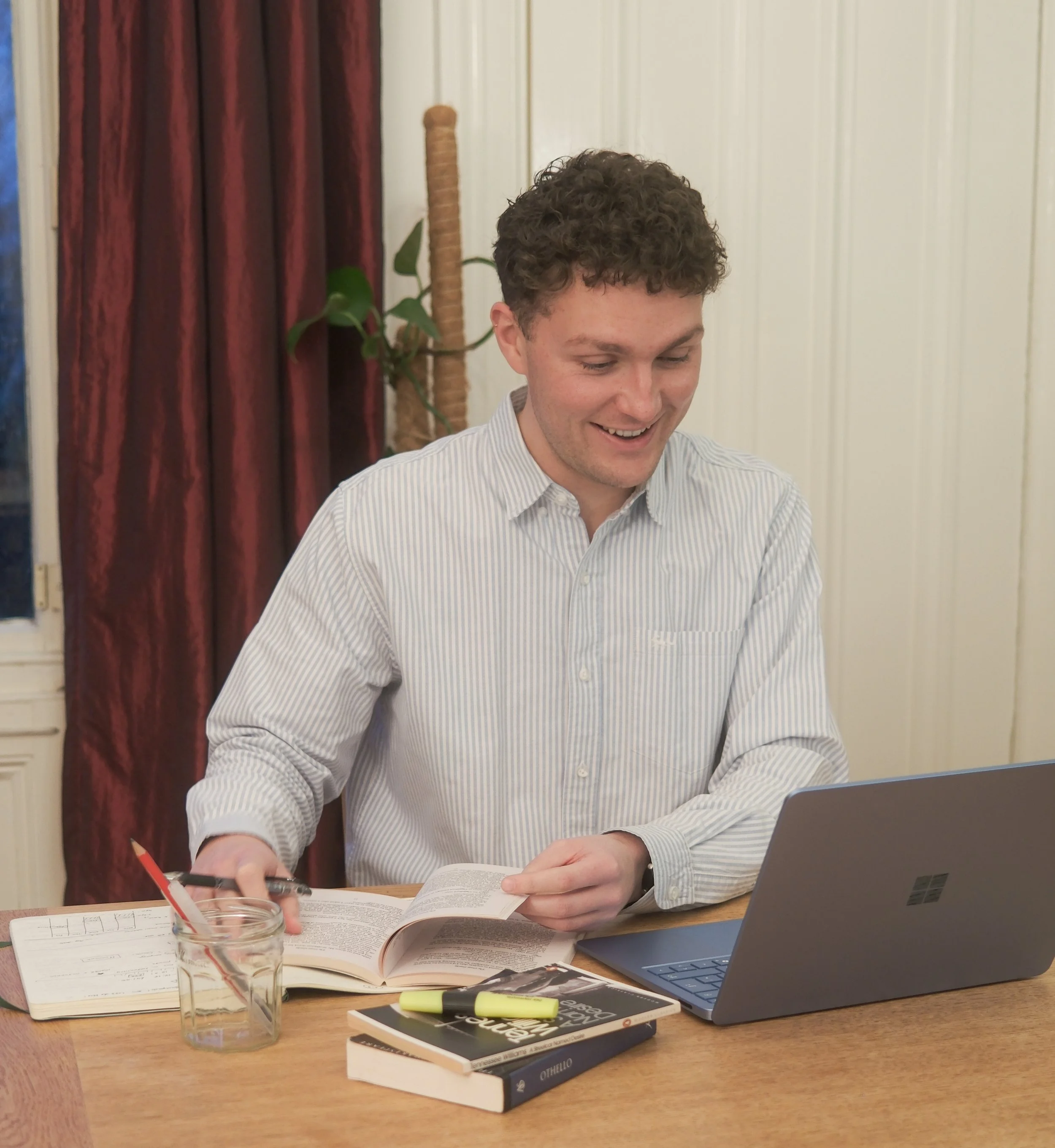 A friendly English tutor at a wooden desk providing 1-1 personalised English tutoring lessons to GCSE and A Level pupils via a laptop in order to help them attain a top grade.