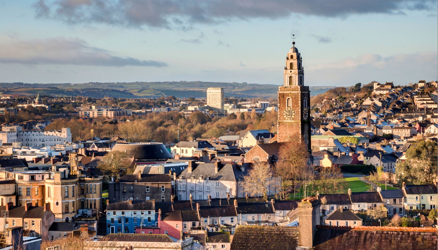 Cityscape of a European town with a prominent clock tower church in the foreground, residential buildings, and hills in the background.