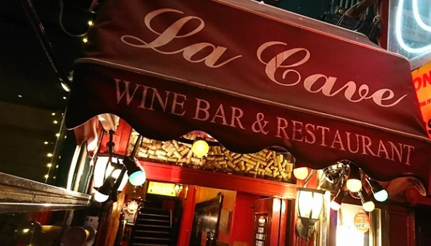 Exterior of a restaurant with a red awning reading "Lav Cava Wine Bar & Restaurant" and festive string lights hanging outside.