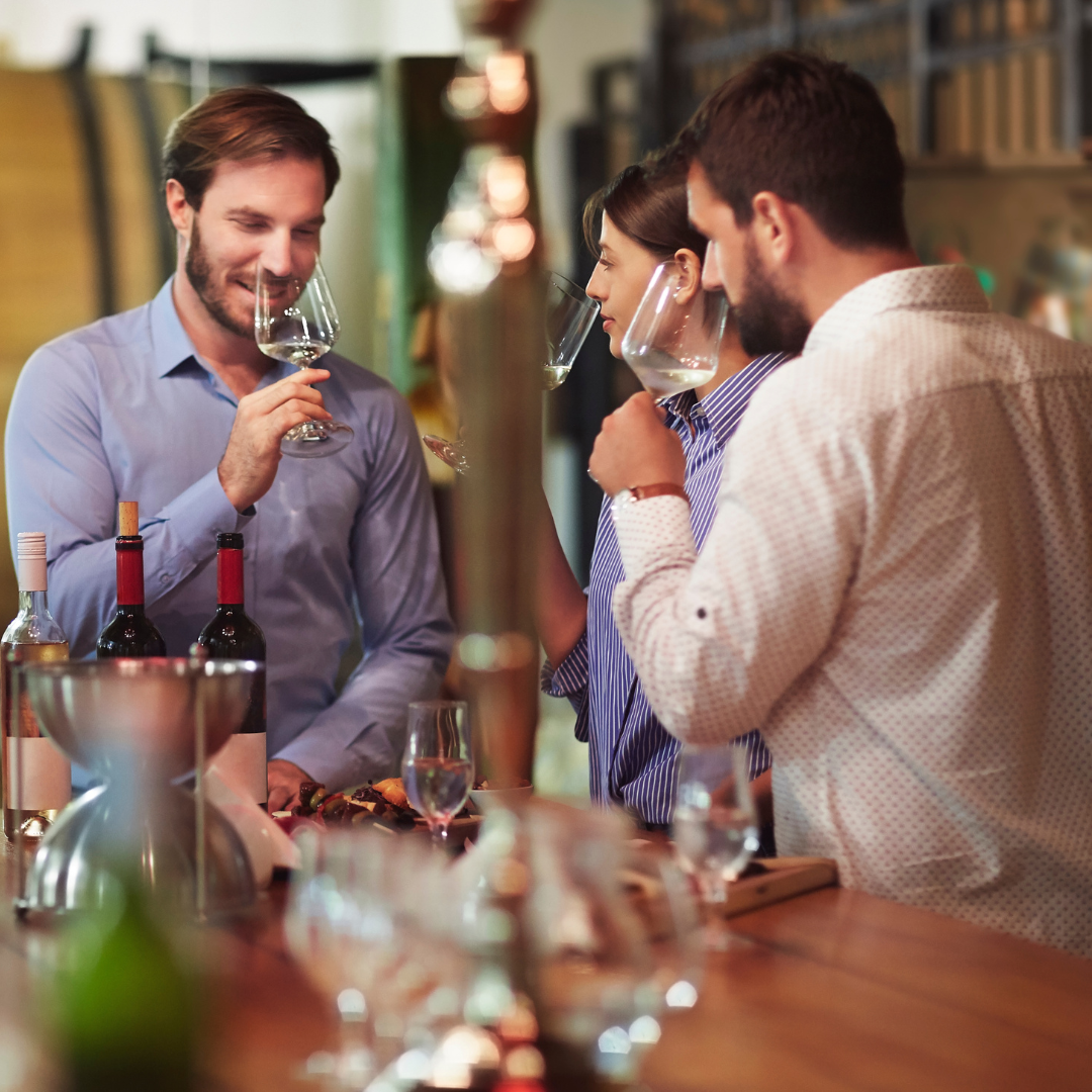 Two men and a woman sniffing and sipping wine in a wine tasting room