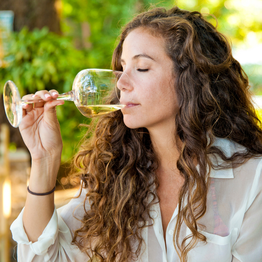 Woman with long curly hair sips white wine in a vineyard