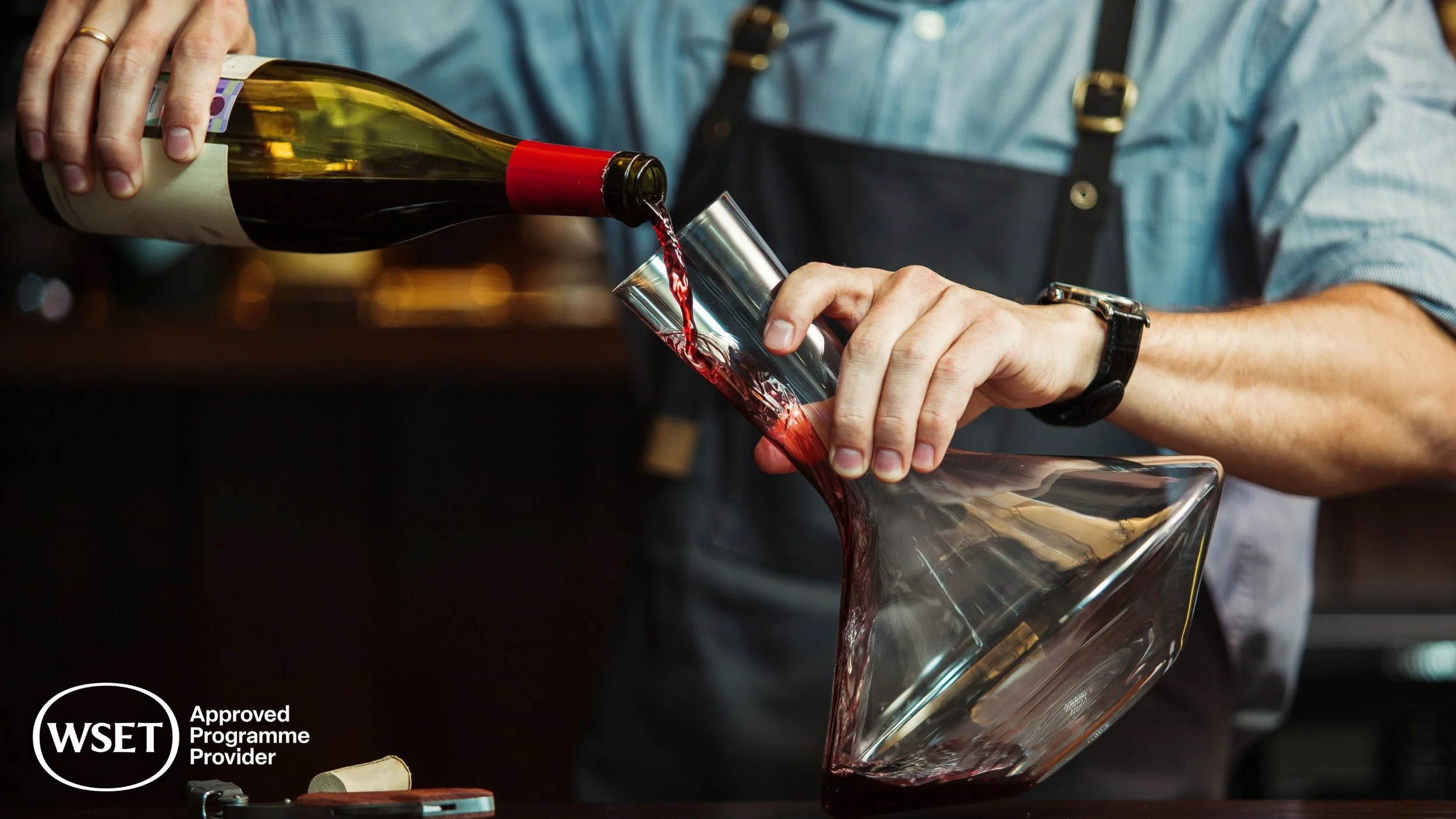 Person pouring red wine from a bottle into a glass vessel.