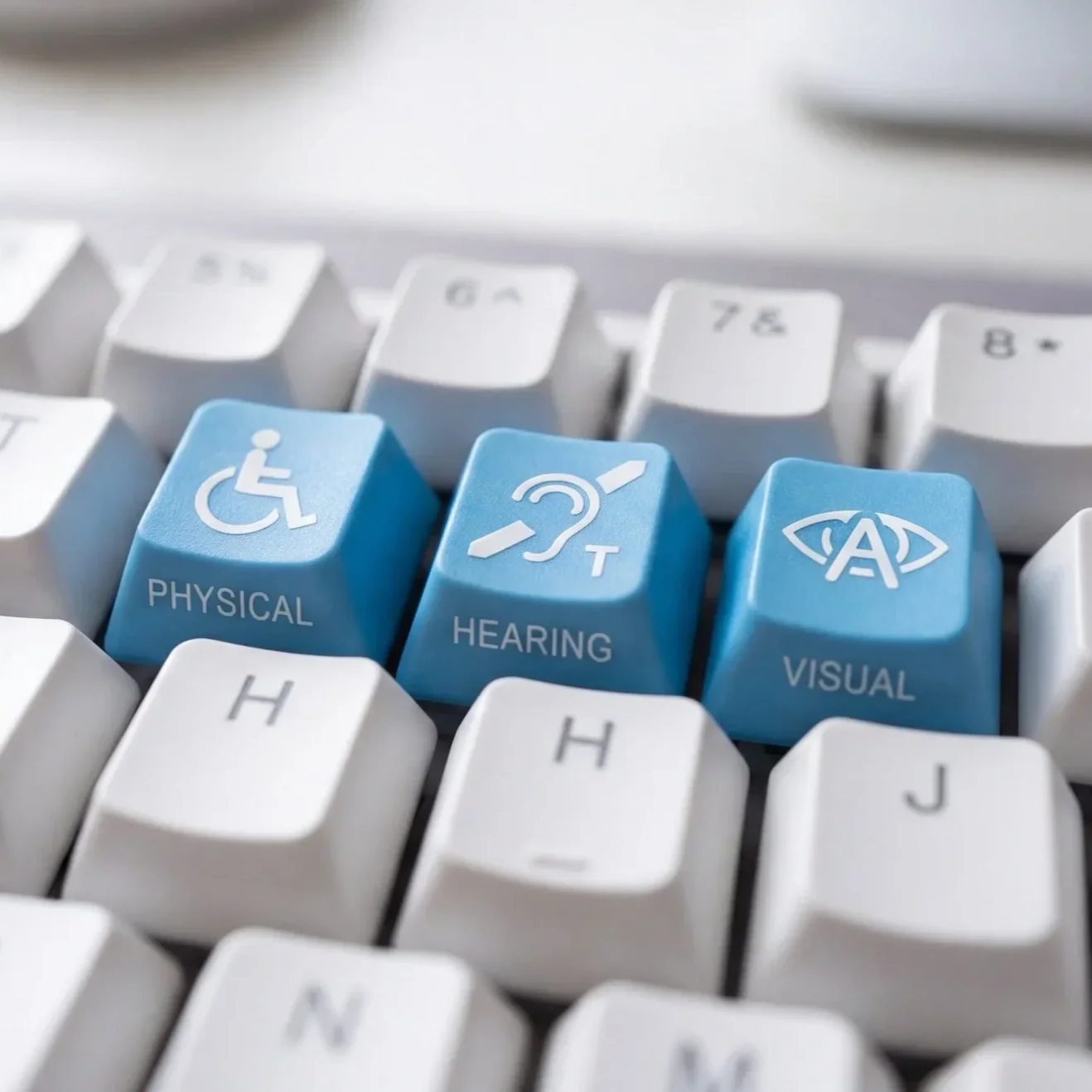 Close-up of a computer keyboard with three blue keys labeled Physical, Hearing, and Visual, featuring accessibility icons.
