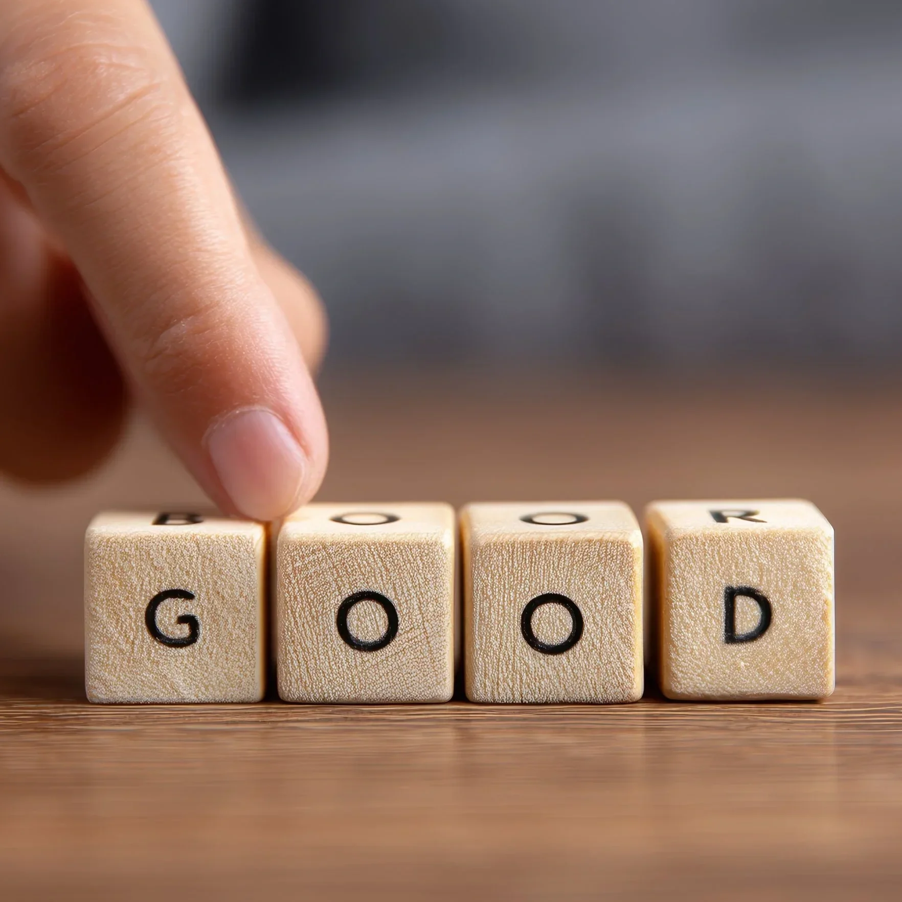 Close-up of a person's finger pointing at wooden letter tiles spelling out the word "GOOD".