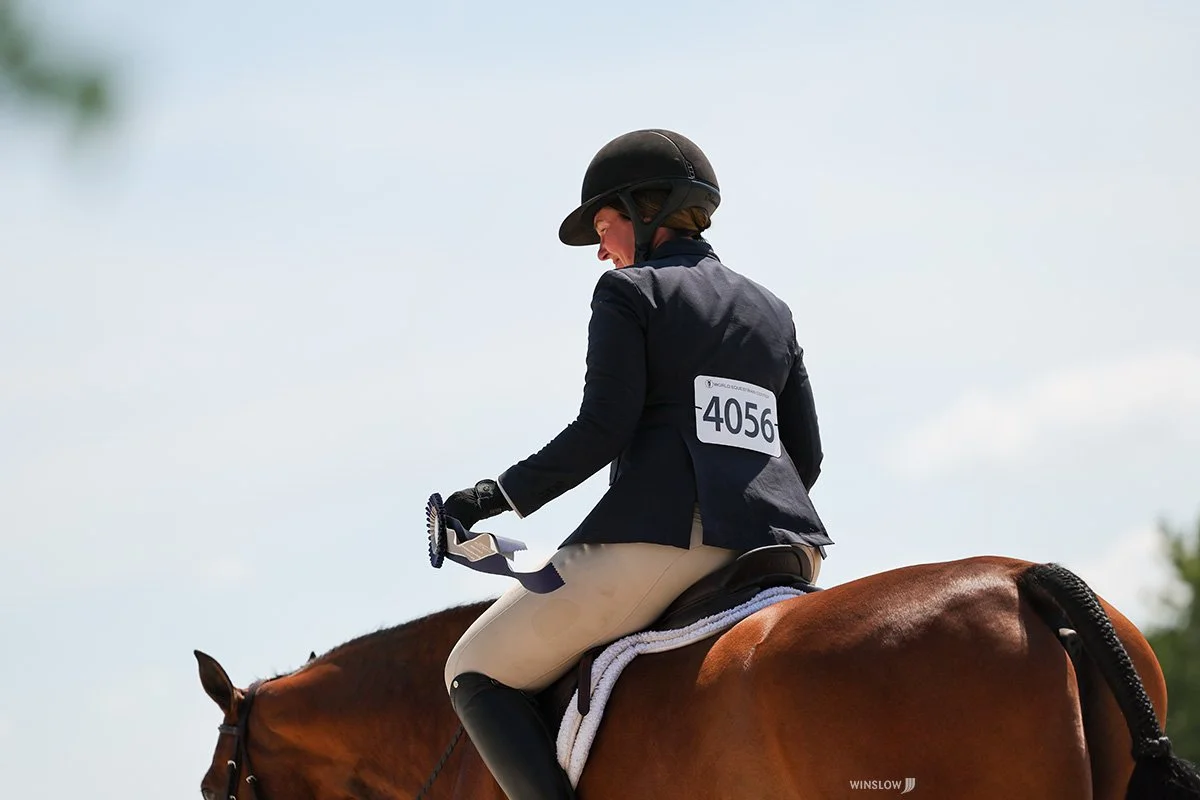 A woman riding a brown horse during a competition with the number 4056 displayed on her back, wearing a black helmet and riding attire.