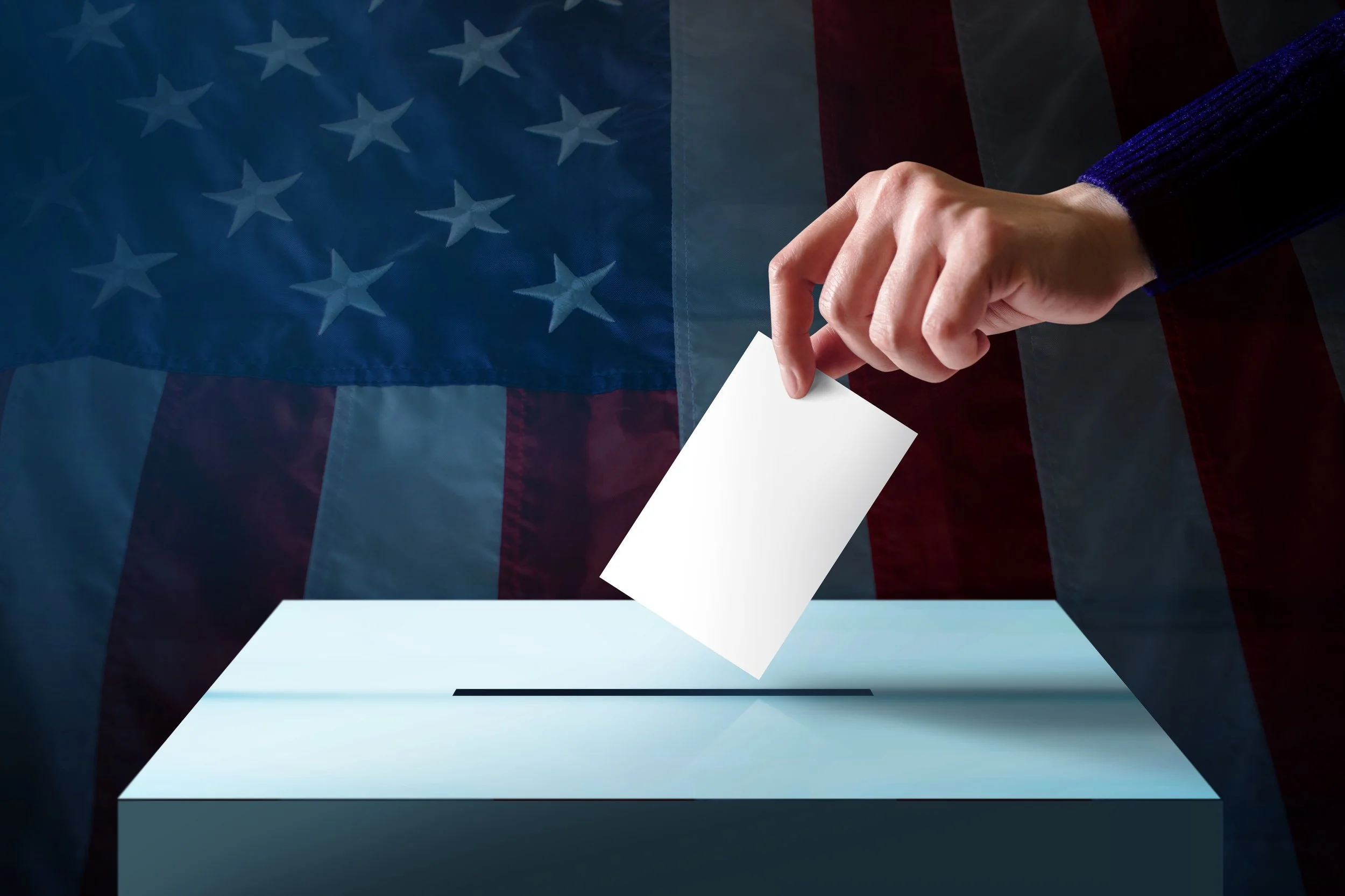 A person placing a ballot into a ballot box with an American flag in the background.