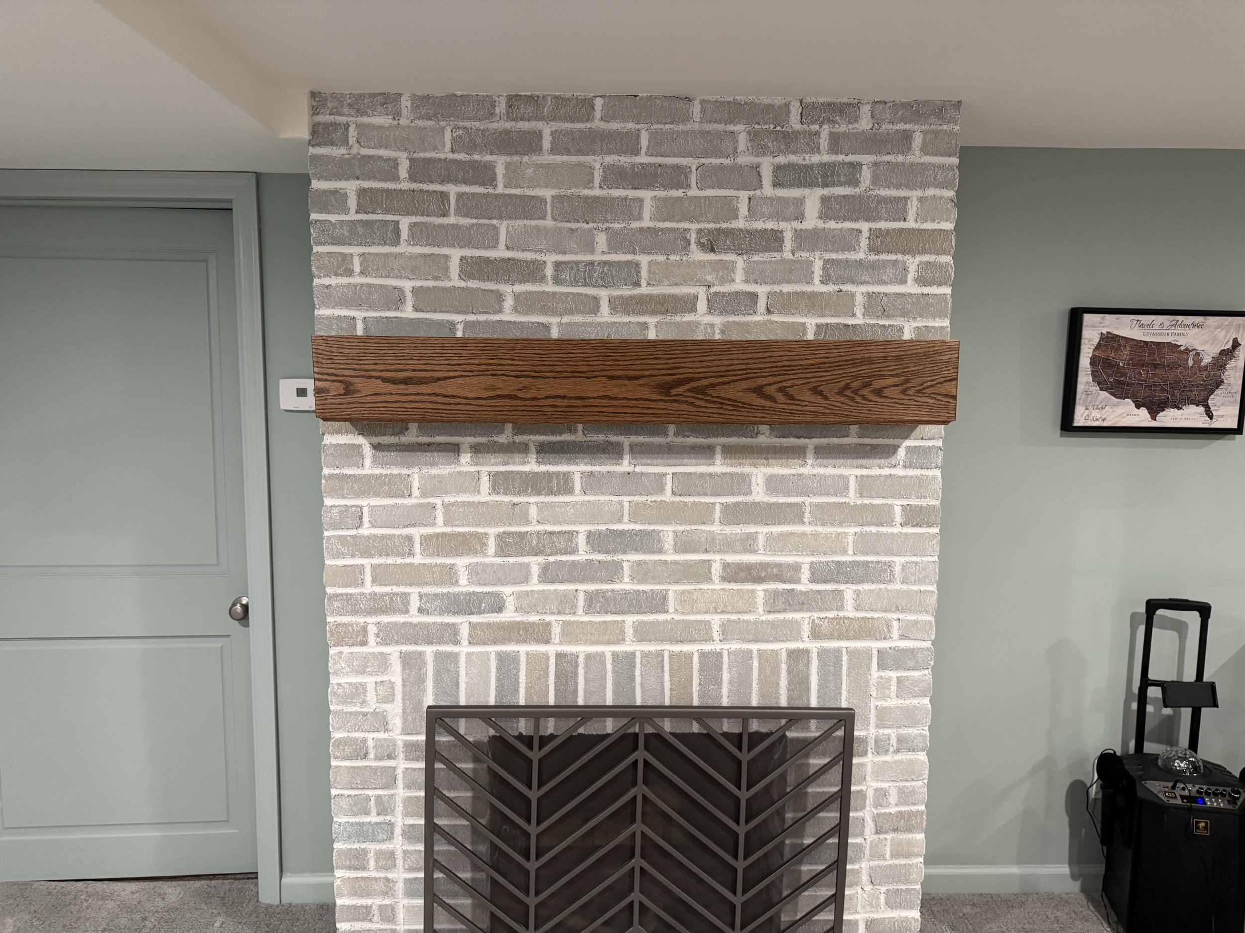 A white brick fireplace with a wooden mantel, set against a light green wall. To the right, there is a picture of the United States map and some electronic equipment with a music stand.