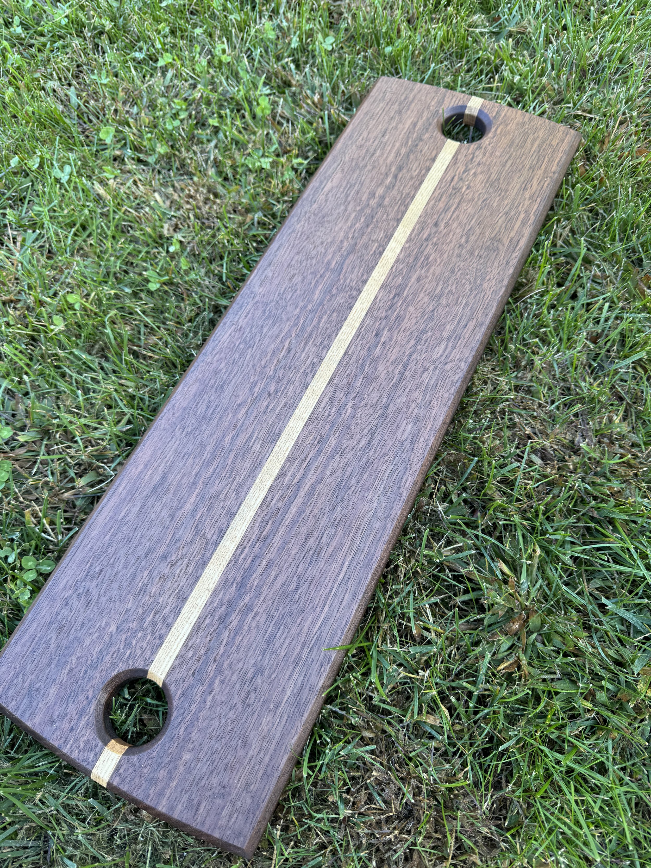 Wooden Charcuterie board made of walnut and maple, placed on grass field.