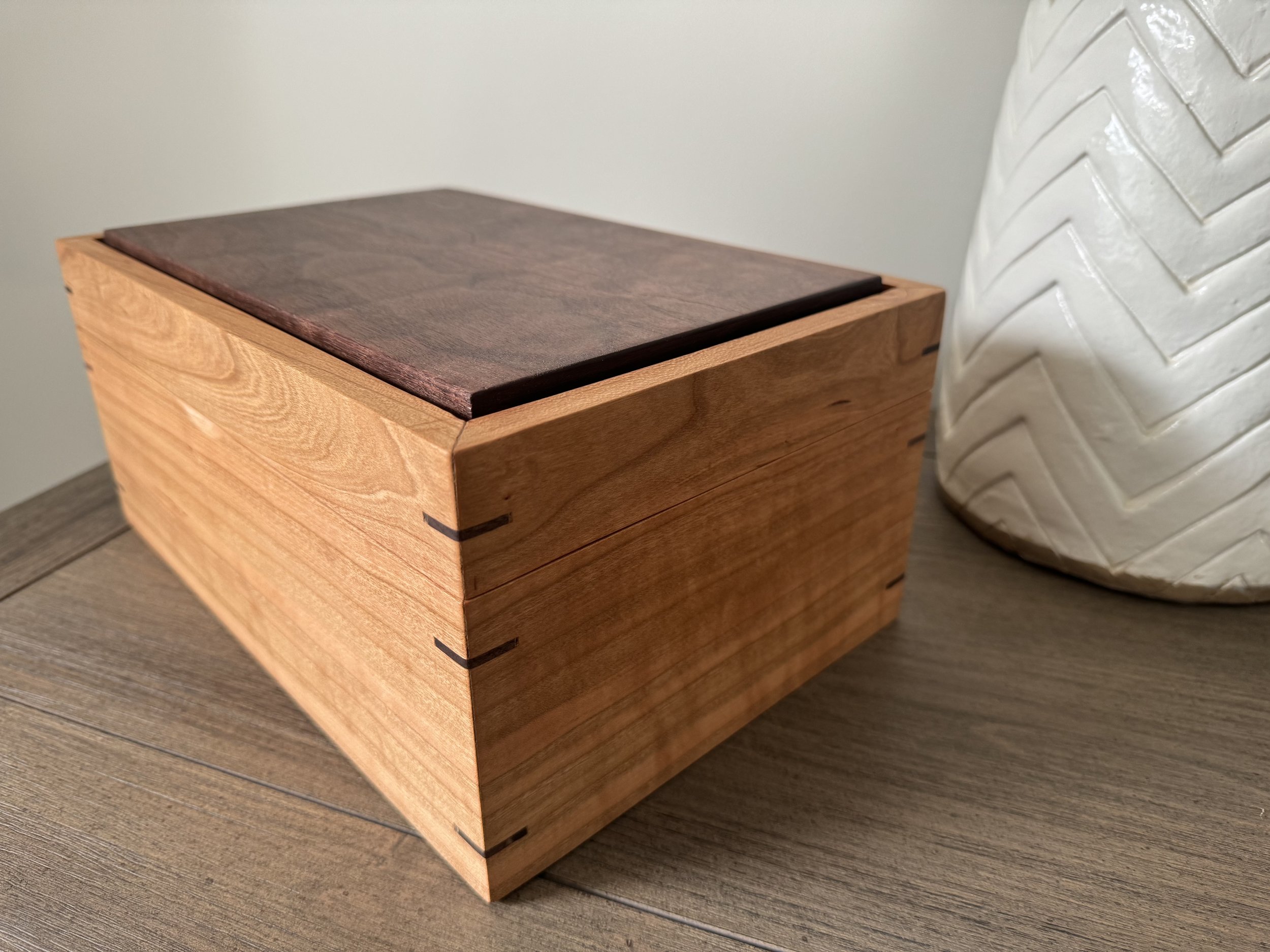 A wooden cherry box with dovetail joints, sitting on a wooden surface.