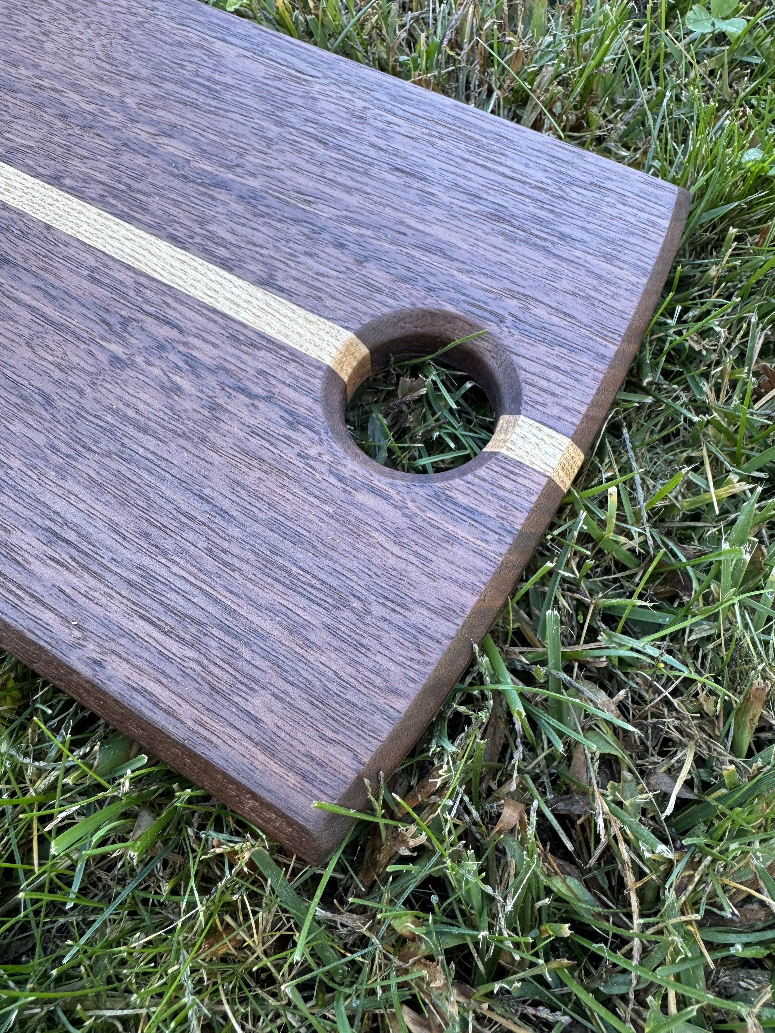 Close-up of a wooden serving board with a hole in it, placed outdoors on grass.
